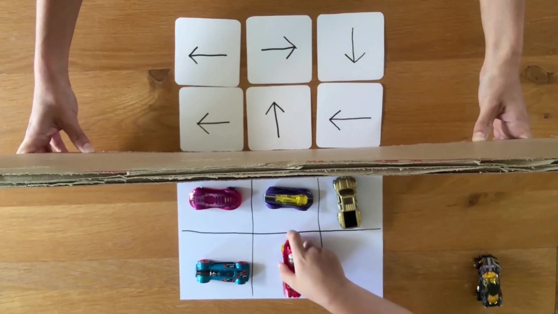 Cardboard held between an arrow grid and a blank grid where a child is placing cars to match the memorised arrow grid.