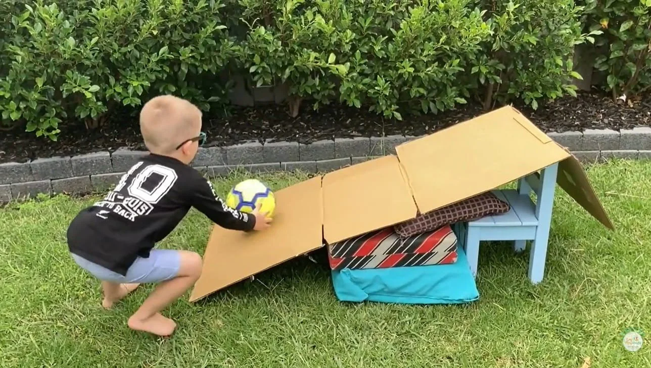 Child catching a ball at the bottom of a ball ramp as part of an obstacle course