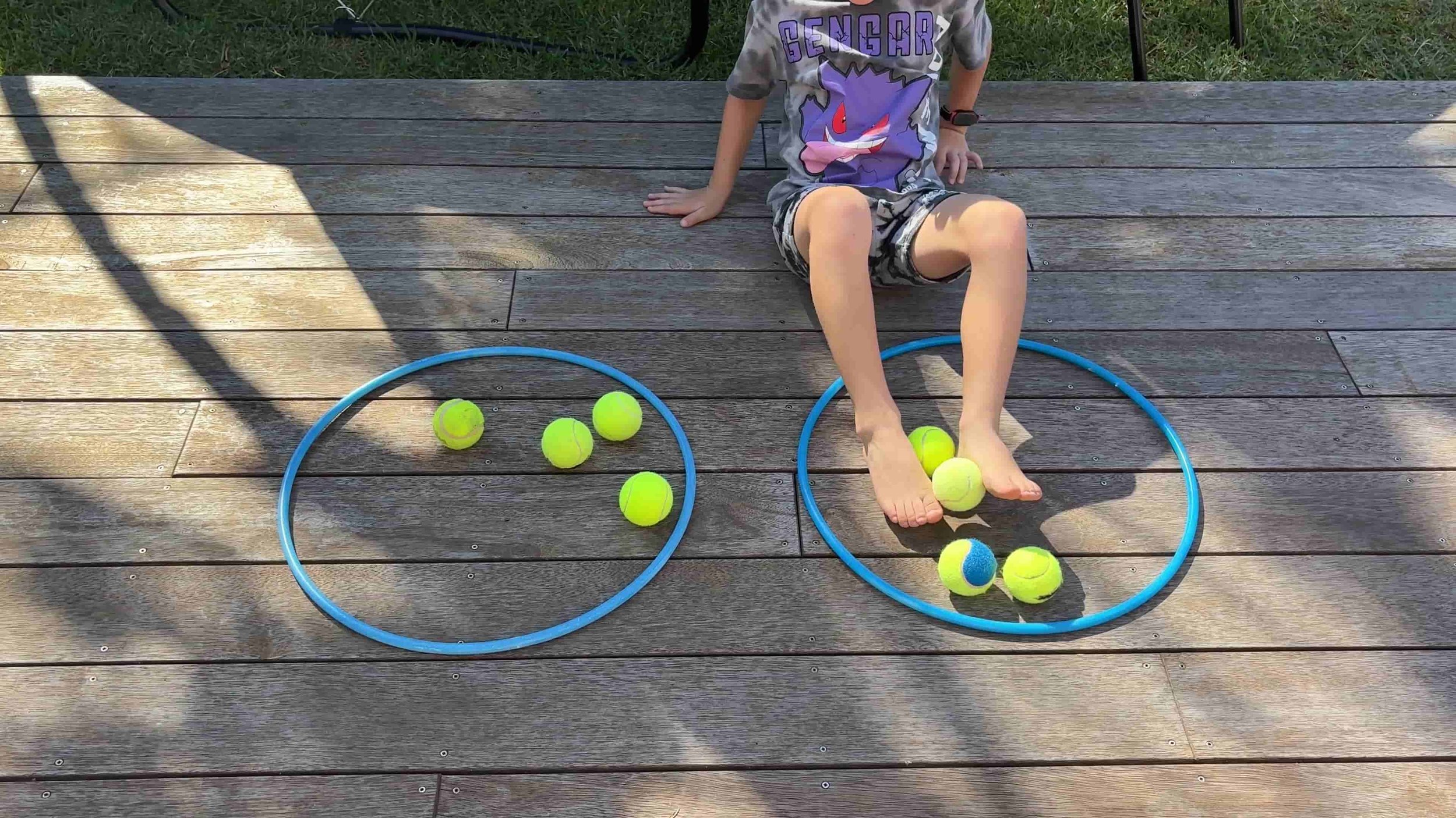 Child picking up tennis balls from one hoop then putting it into the next hoop with their feet