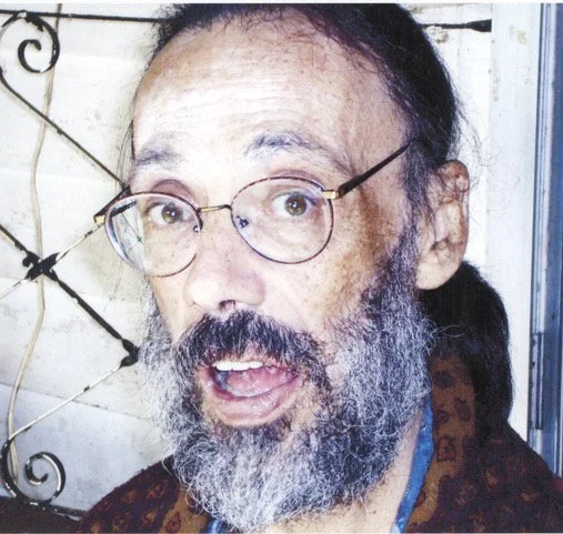 A man with glasses and a beard, with long hair tied back, looking surprised or confused.