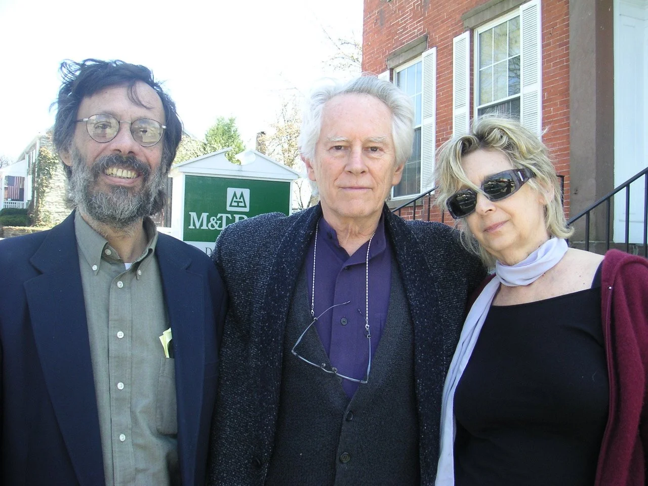 Three people standing outside in front of a building with a sign that reads M&T Bank, smiling at the camera.