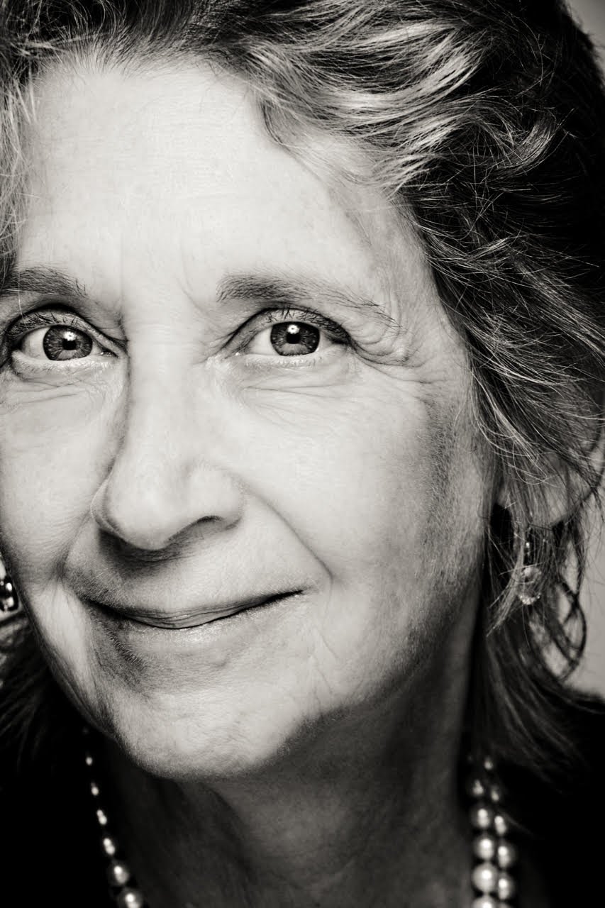 Black and white close-up portrait of a joyful older woman with gray hair, wearing pearl earrings and a pearl necklace.