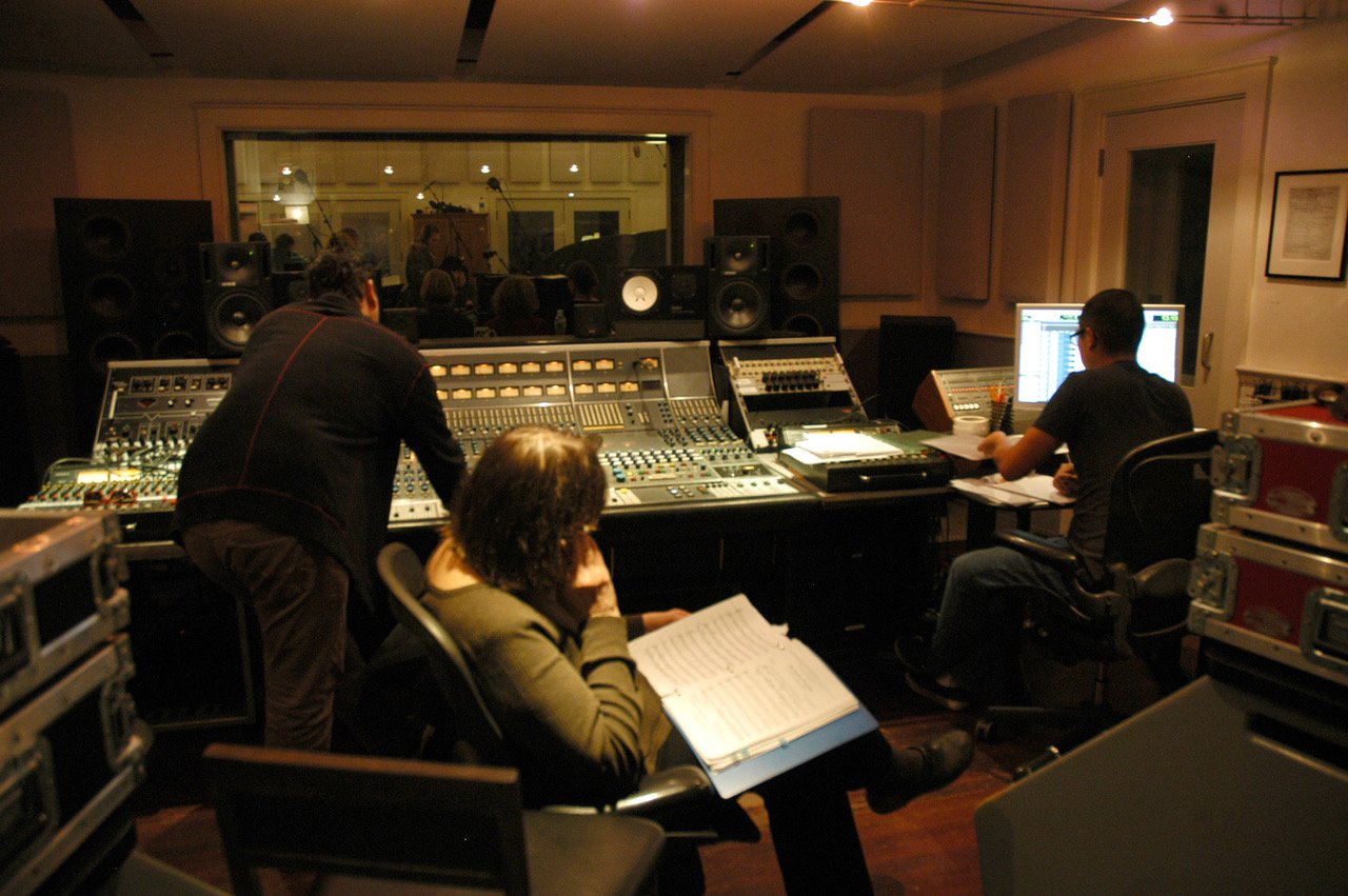 Recording studio with sound engineers working on mixing equipment and computers, with studio monitors and acoustic panels on the walls.