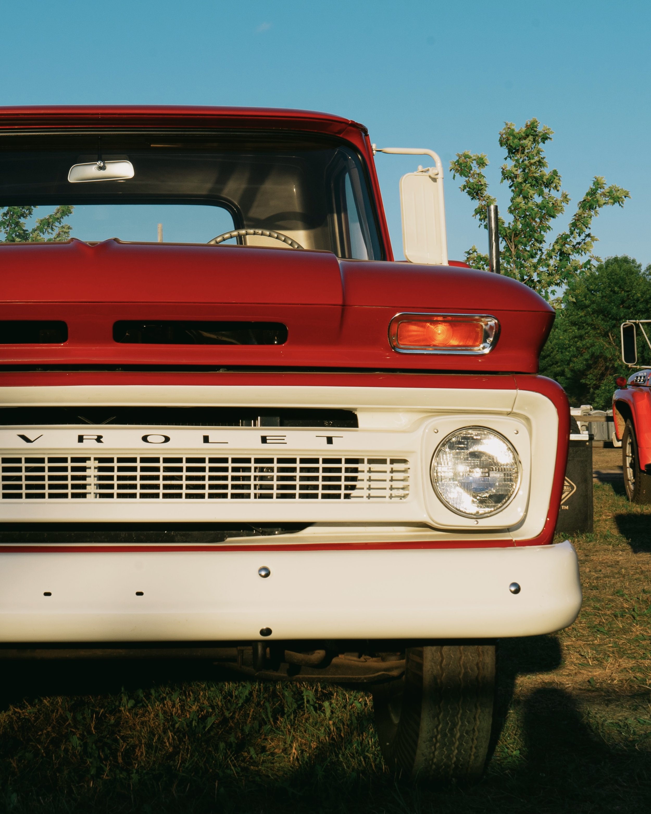 Front view of a vintage red and white Chevrolet truck parked on grass, with a clear sky and trees in the background.