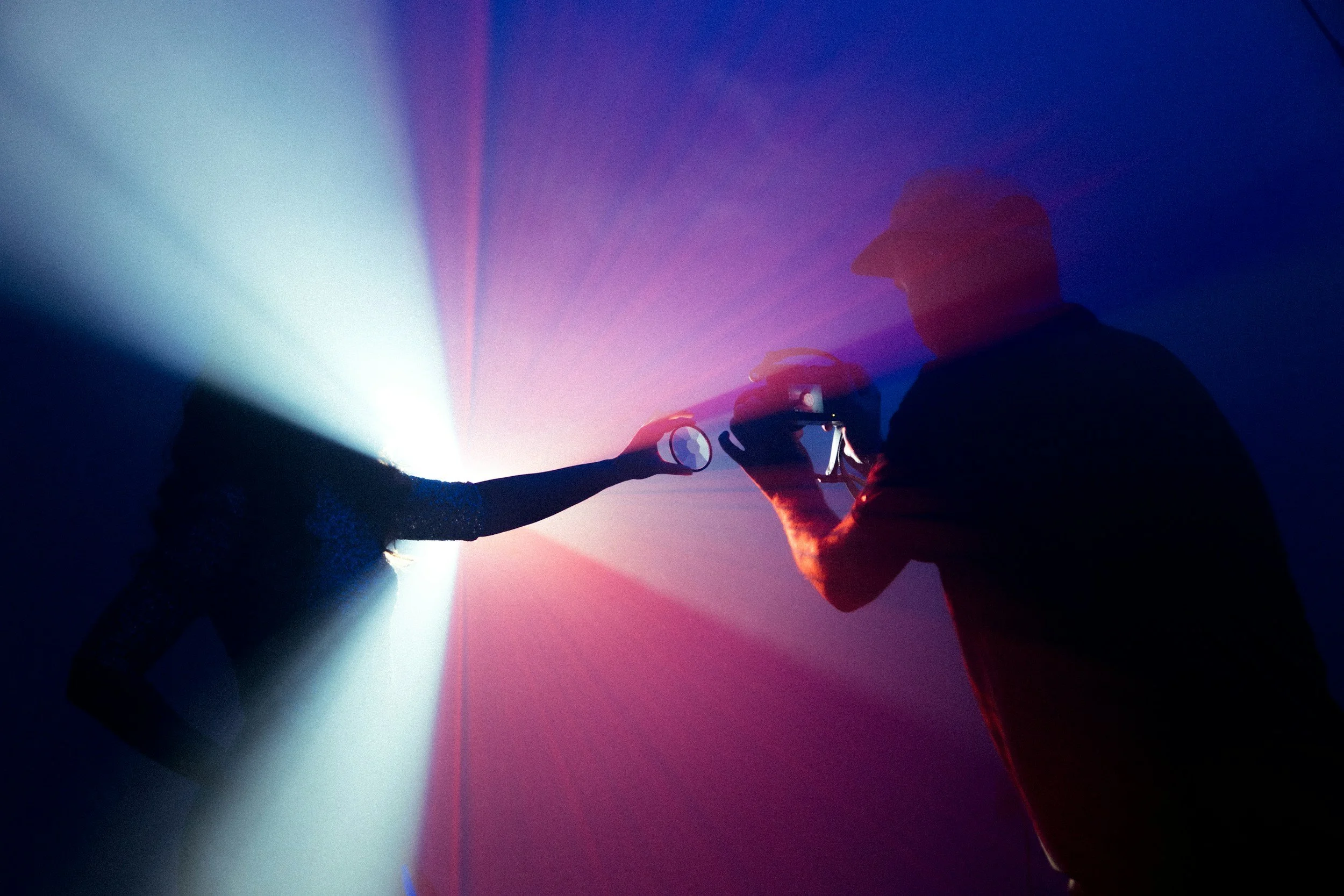 Silhouettes of a woman and a man taking a photo or selfie against colorful stage lighting.