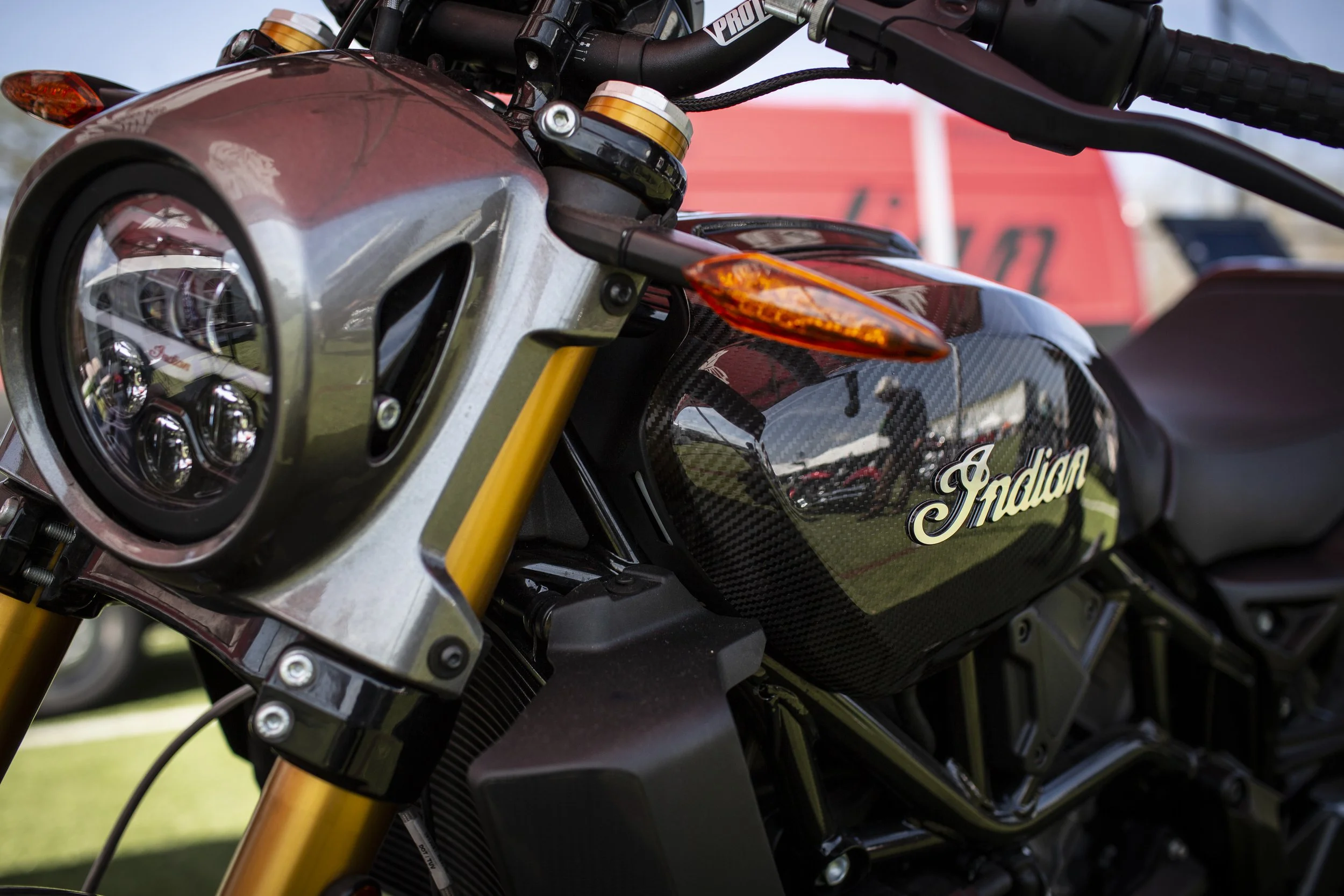 Close-up view of a black Indian motorcycle with carbon fiber accents, gold front forks, and a prominent headlight, parked outdoors.