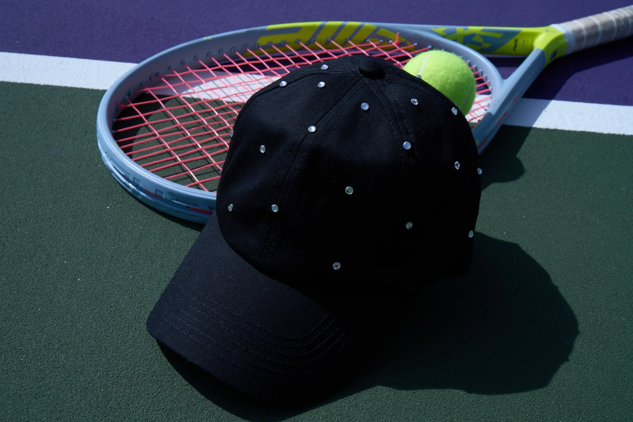 A black rhinestone studded tennis cap by High Spirits on a tennis court