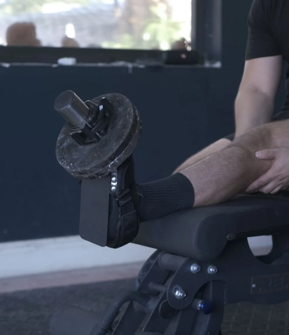A person performing a leg exercise on a leg curl machine at the gym, with a weight disc attached to their ankle