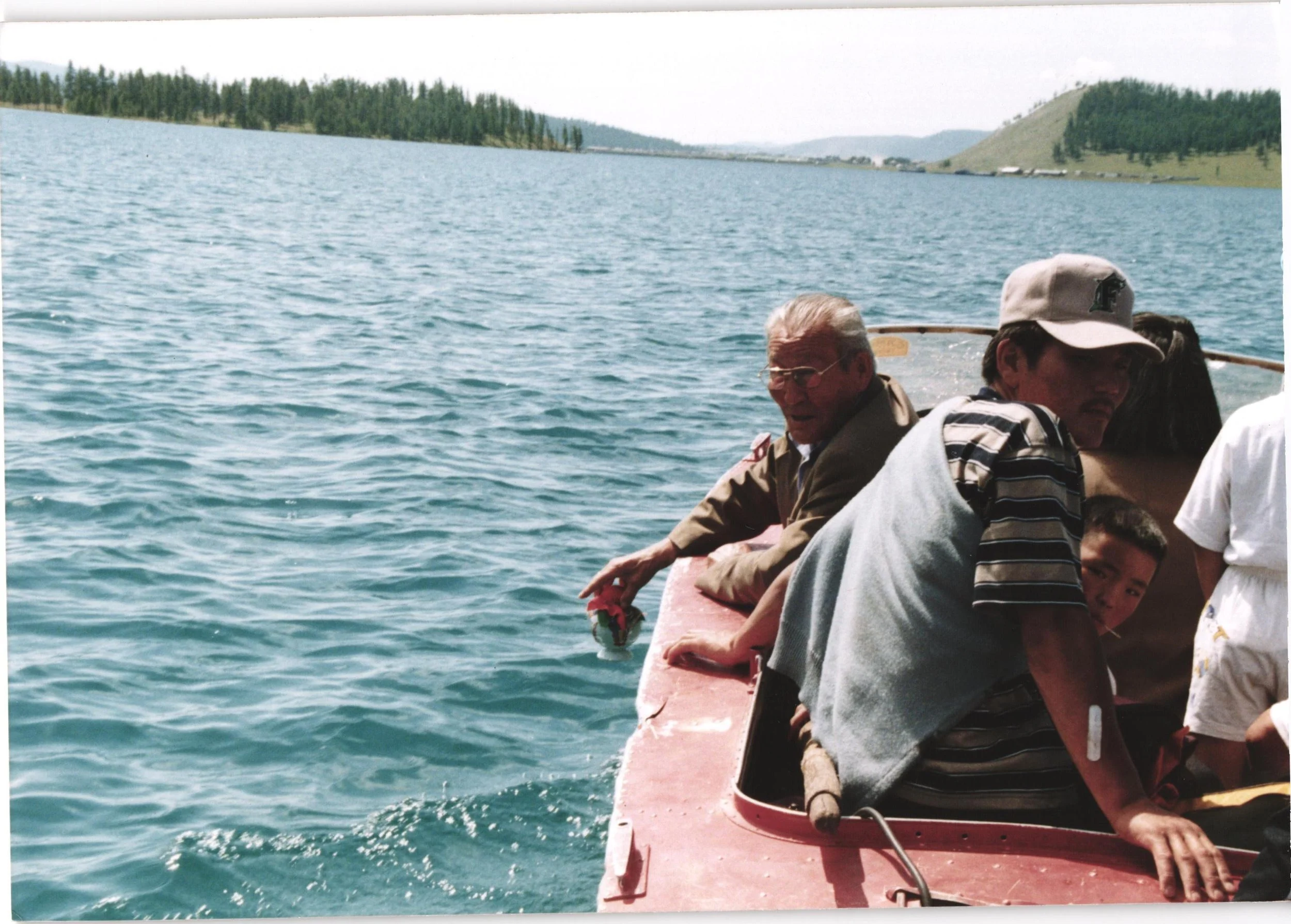People sitting on the edge of a boat on a lake with forested hills in the background.