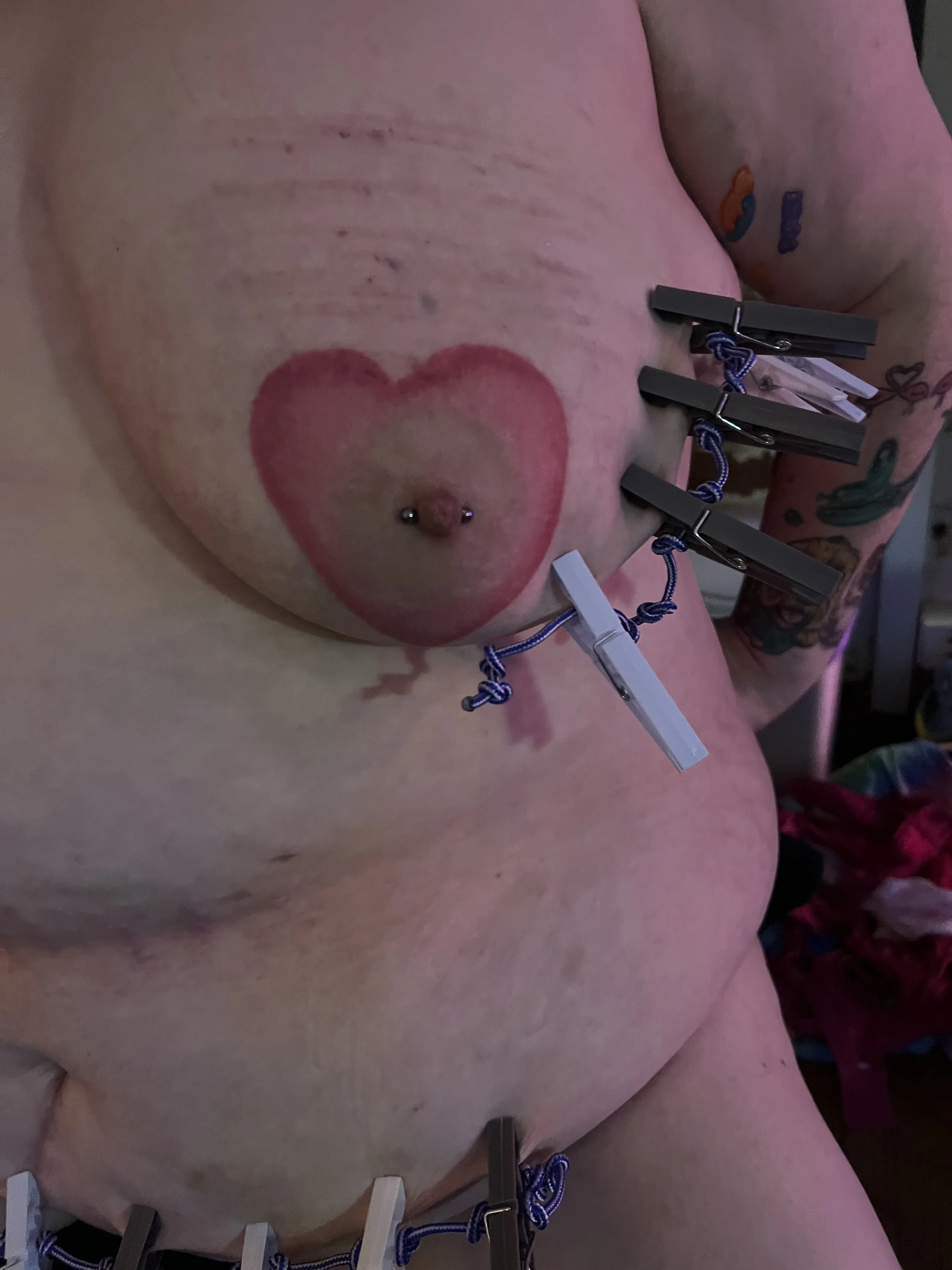 Breast and tummy adorned with clothes pegs, wire, and clamps