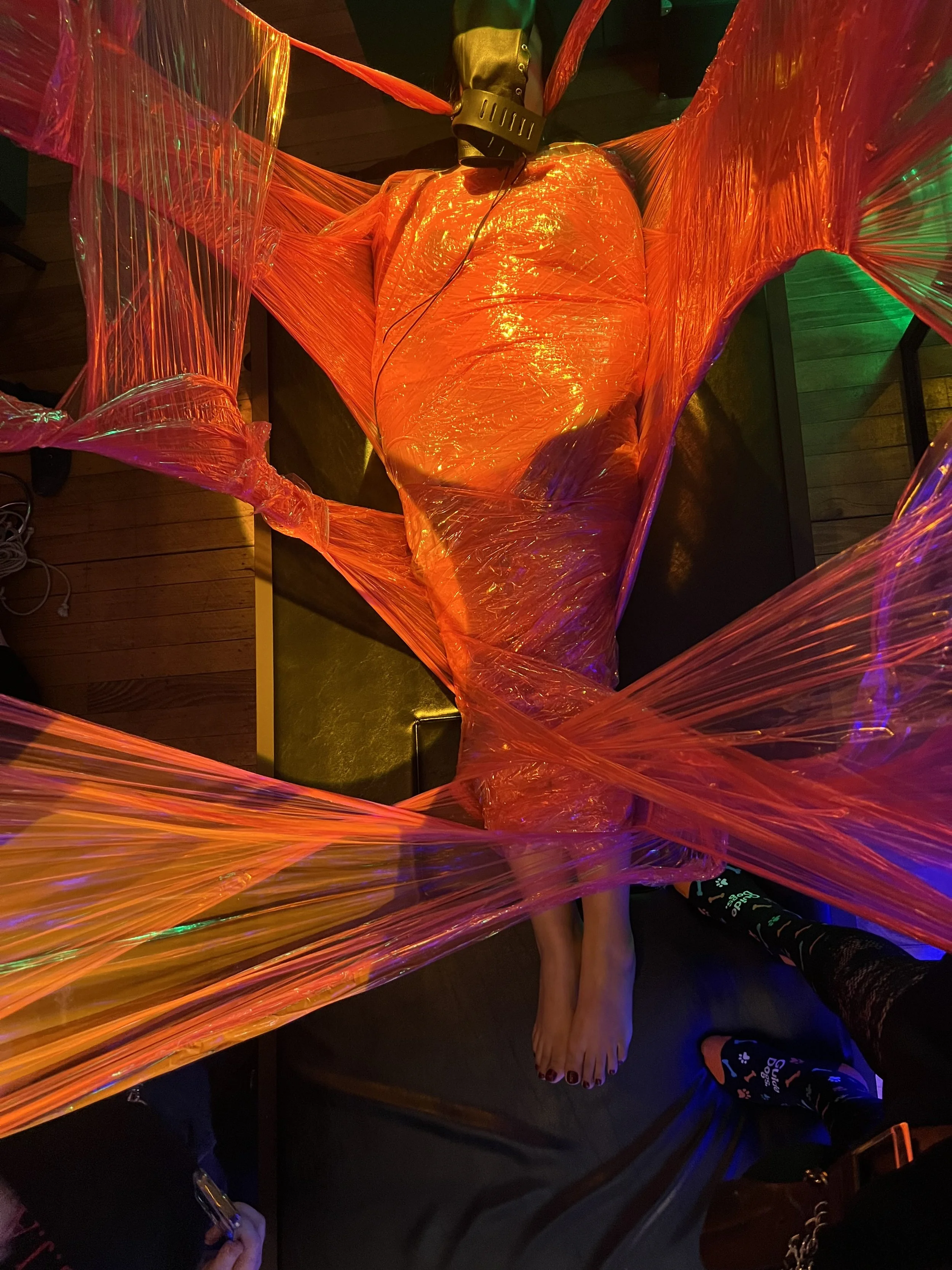 Person suspended in red saran wrap