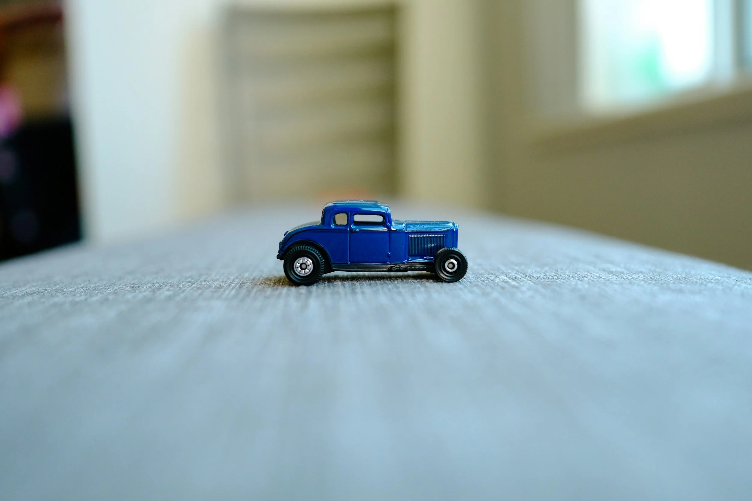 A small blue toy car on a textured surface with a blurred indoor background.