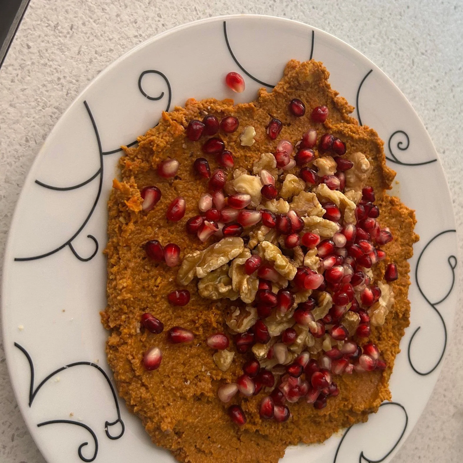 Muhammara – syrisk peberfrugtdip toppet med valnødder og granatæblekerner på en hvid tallerken