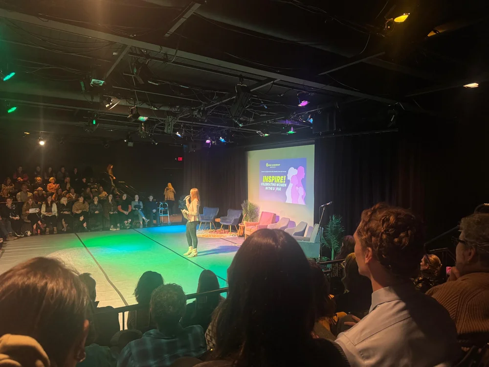 Angie speaking on stage to a full room