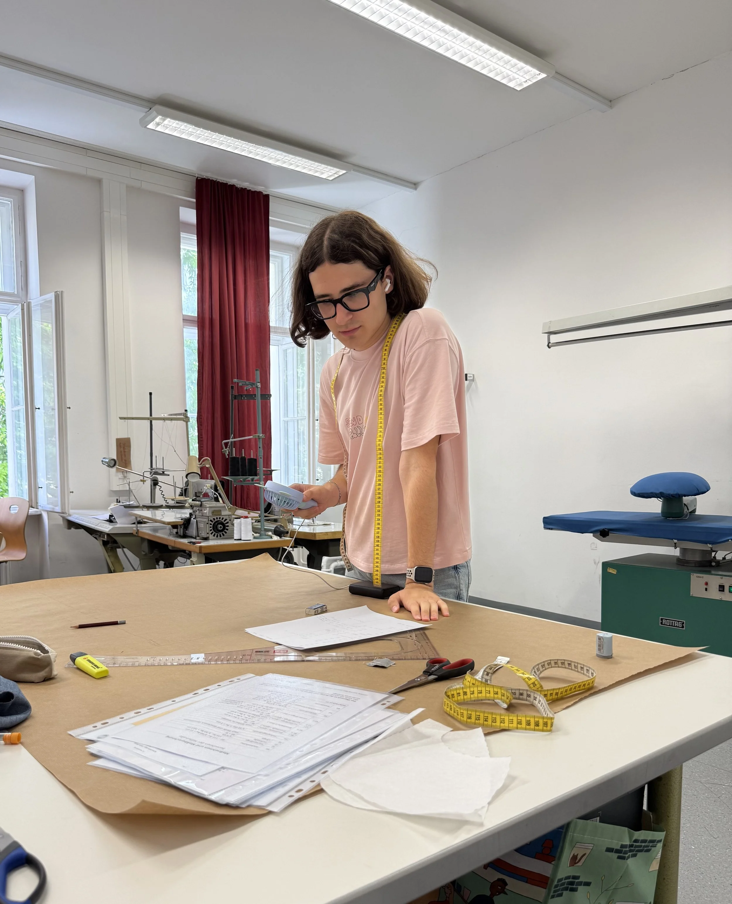 Bogdan in der Werkstatt seiner Schule. Er hat ein Maßband um den Hals und arbeitet an einem Papierschnitt.