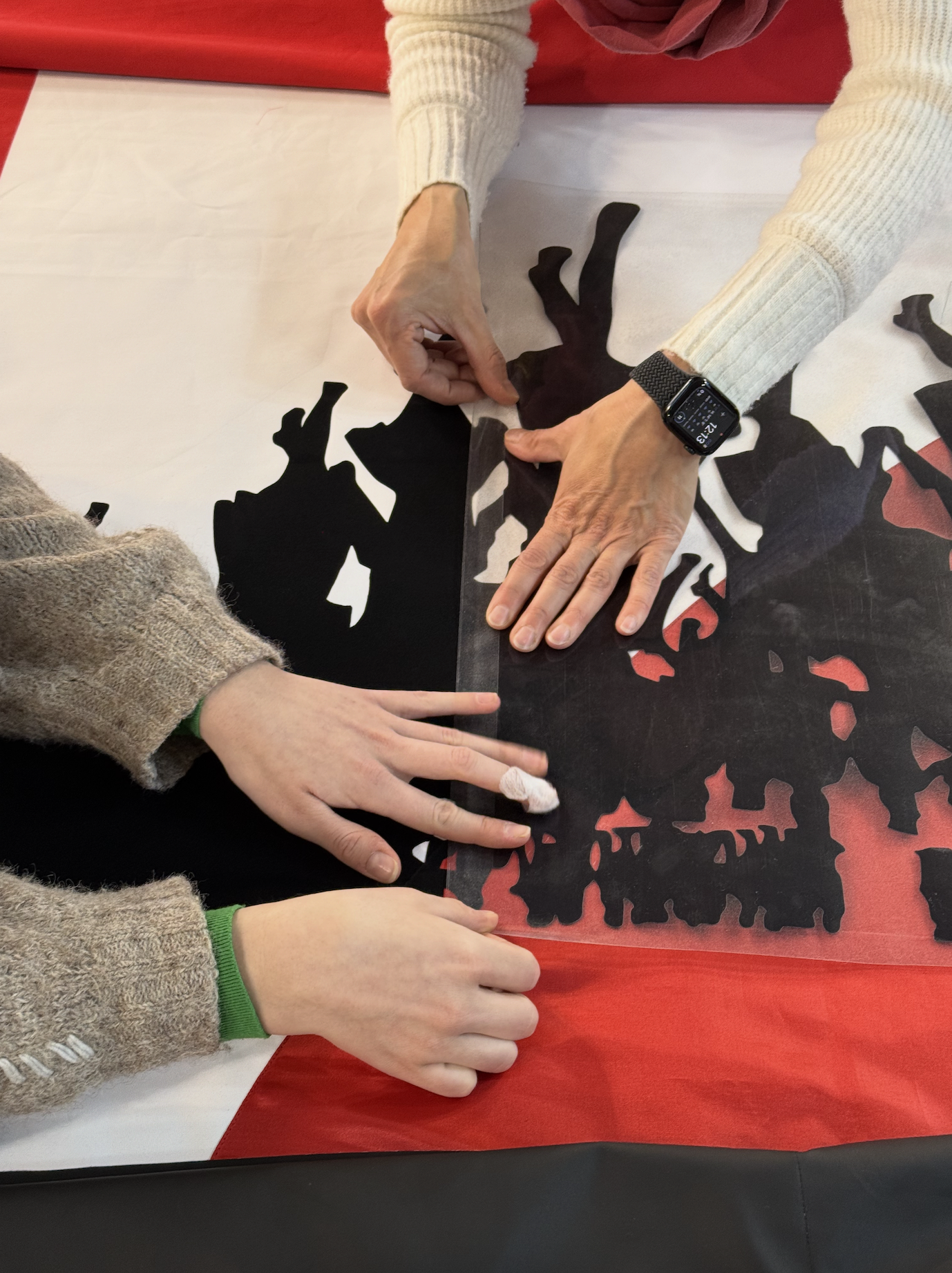 KÖR: 4 Hände platzieren schwarze Flock-Druck-Folie auf einem weiß-roten Banner