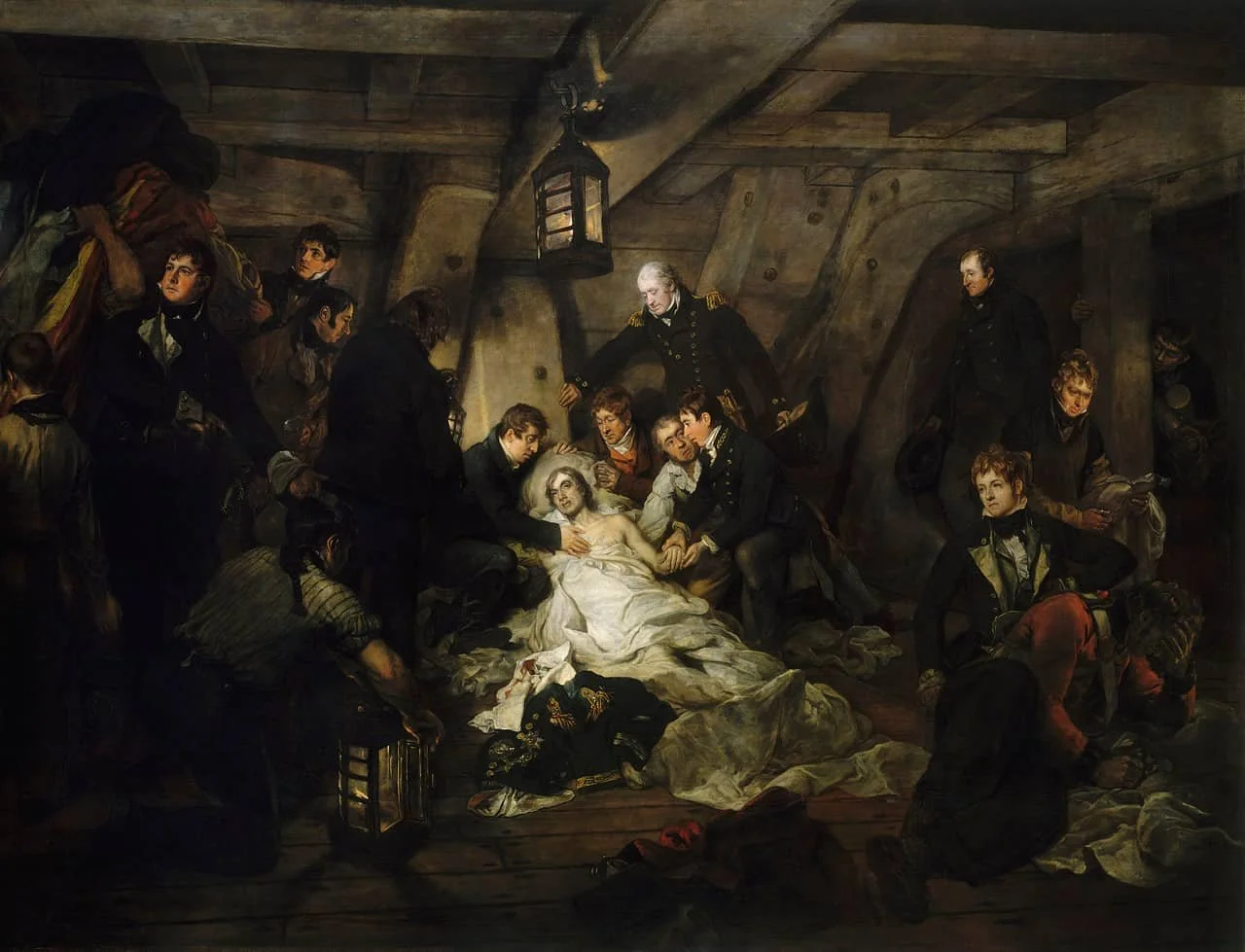 Painting of Nelson, well lit and draped in a white sheet, lying on the floor of the orlop with a halo-like pillow behind his head. The rest of the space is dingy, and about ten other officers are there