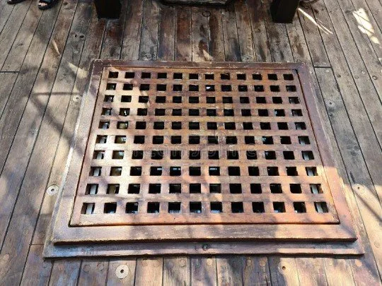 A latticed wooden grating nailed into place above a hatch on the deck of a ship.