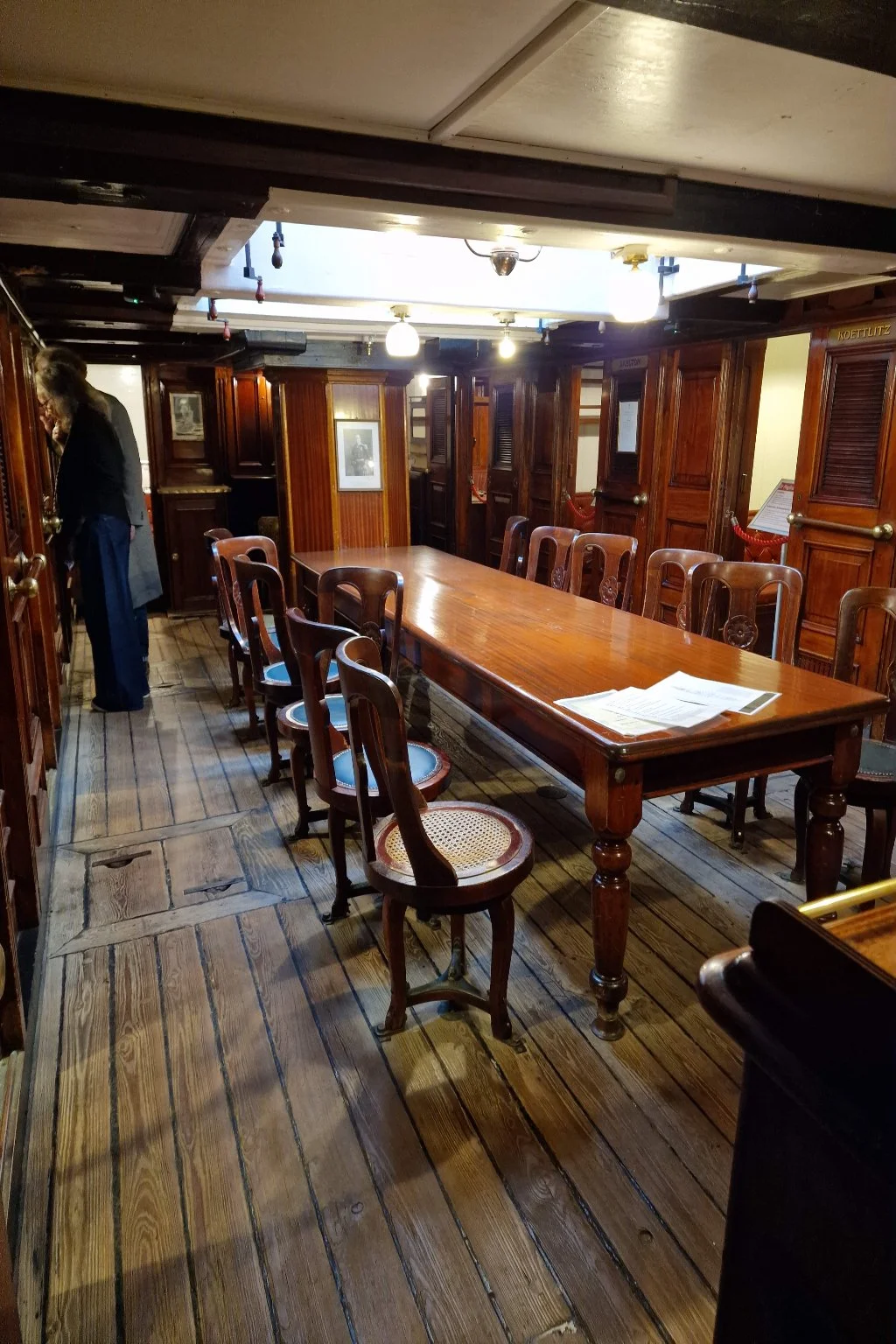 The wardroom. A long (mahogany?) table occupies the central space. It has 12 chairs around it, each fixed to the floor but able to swivel. The cabin doors open directly off the wardroom.