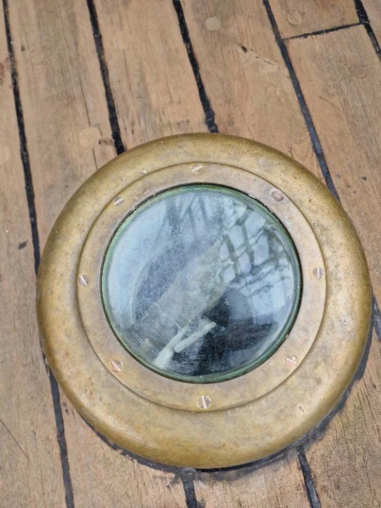 A deck prism seen from above: a brass ring set into the deck, protruding by perhaps a few centimetres, with thick glass within it.