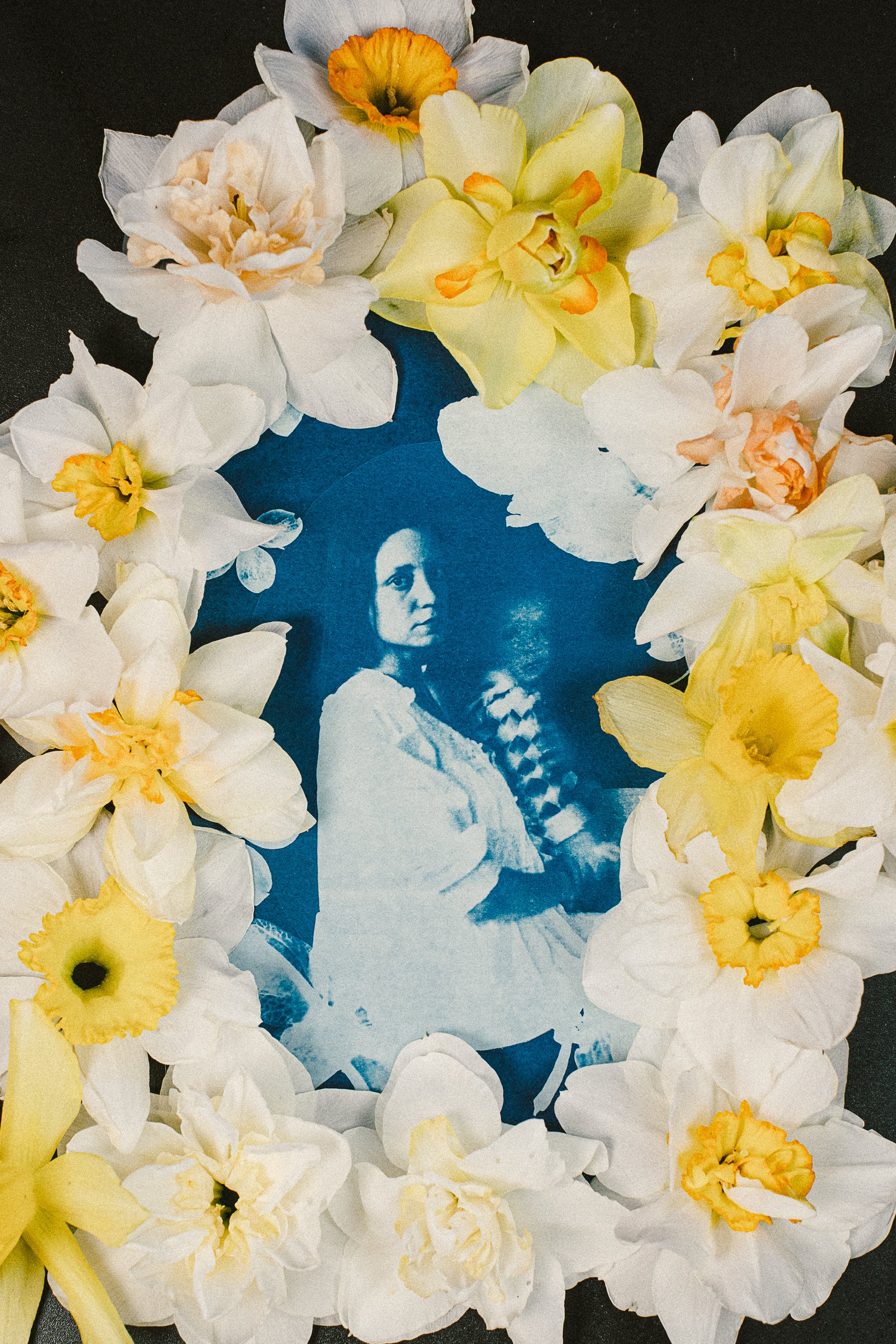 A cyanotype photograph of a woman and baby, surrounded by a frame of daffodils, one of a kind art piece created by hand.