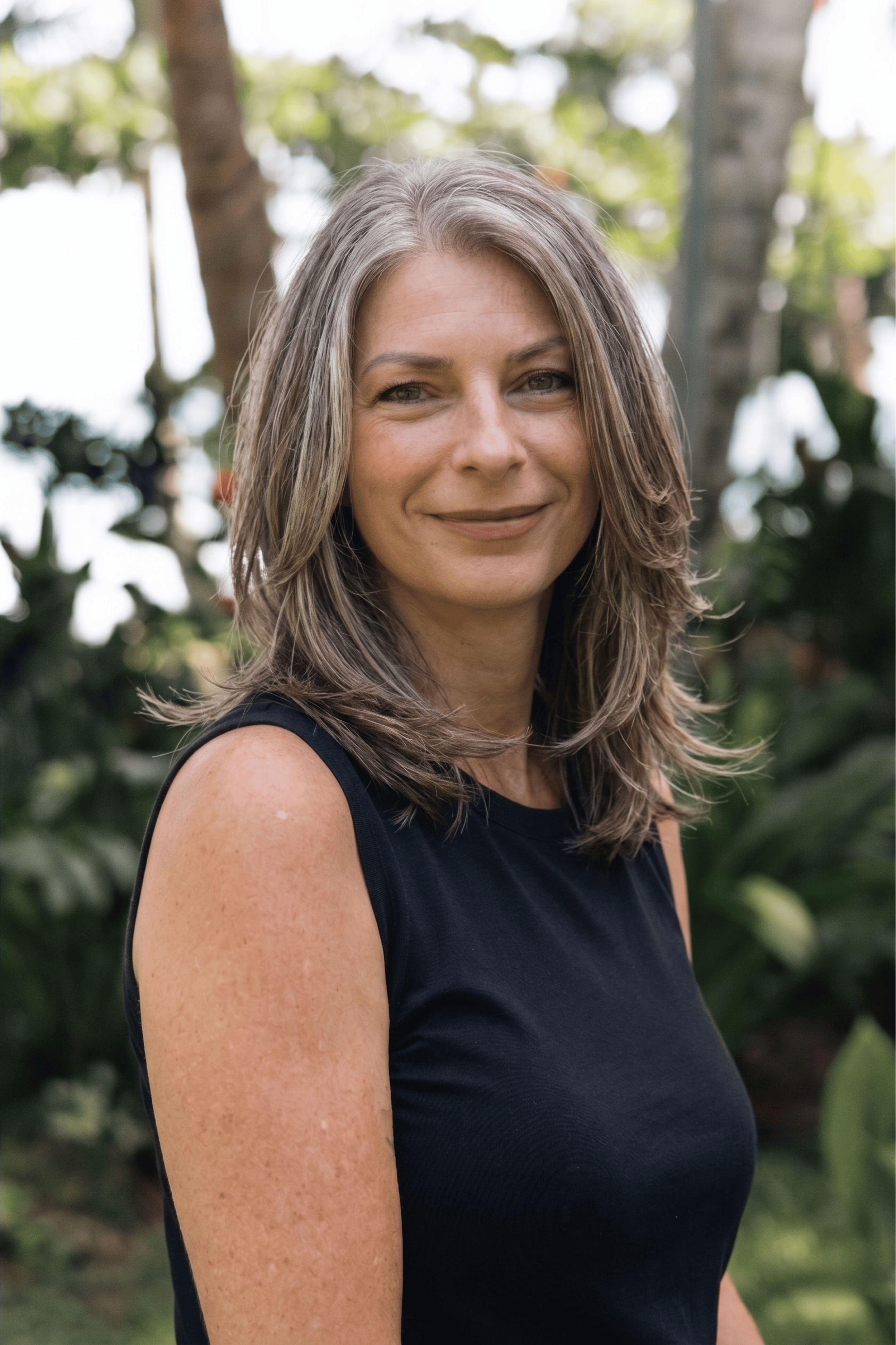 Woman with blank tank top and medium length brown hair in tropical garden