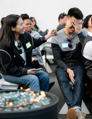 Group of people sitting and laughing at an outdoor event, with one person covering their face in laughter.