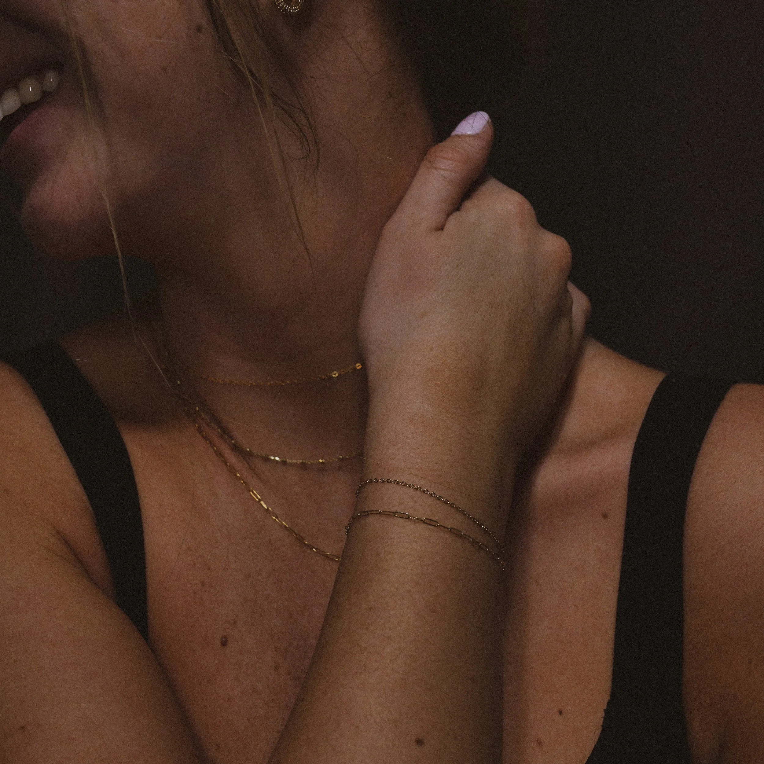 A woman is wearing two gold permanent jewelry bracelets, as well as three gold permanent necklaces.