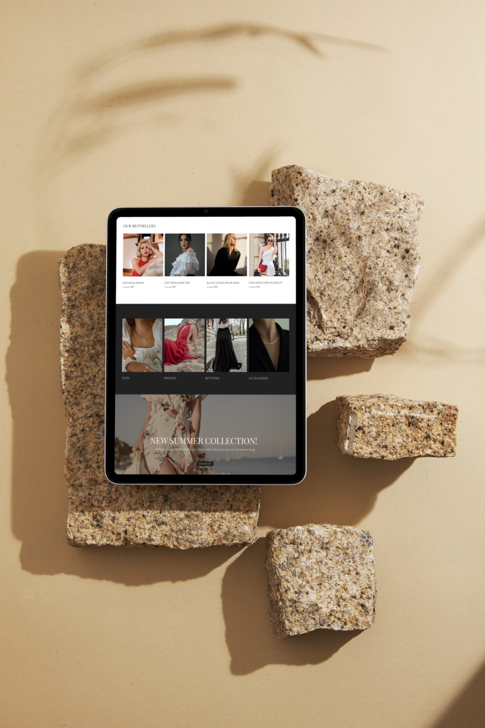 A tablet displaying an online clothing store, surrounded by irregularly shaped rocks on a beige background with shadows.