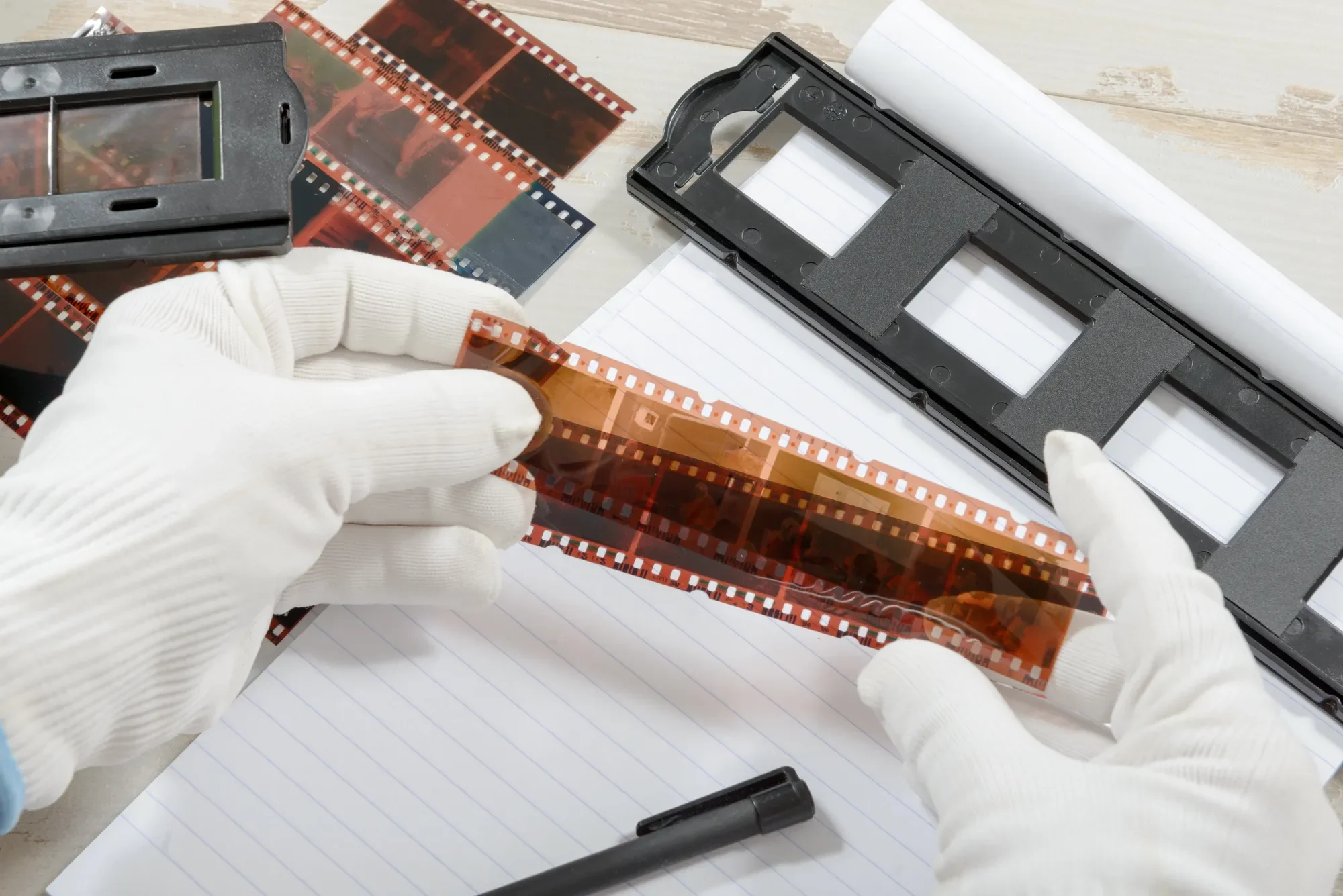 Hands in white gloves handling a strip of film negatives for digital conversion services.
