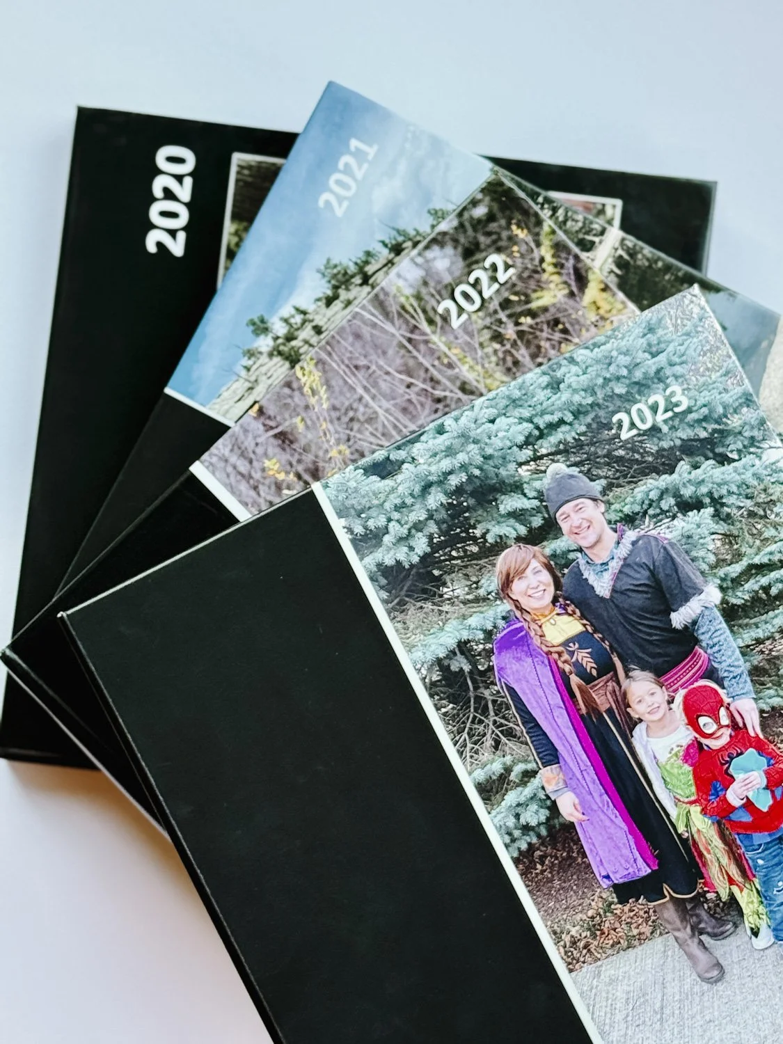 A collection of printed photo books arranged in a fanned-out manner, featuring different cover images and years from 2020 to 2023.