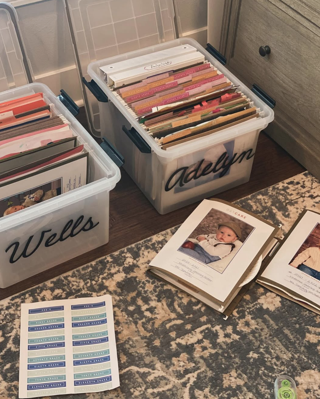 Two clear photo storage bins filled with organized paper files, with organized papers and photo albums on a patterned rug nearby.