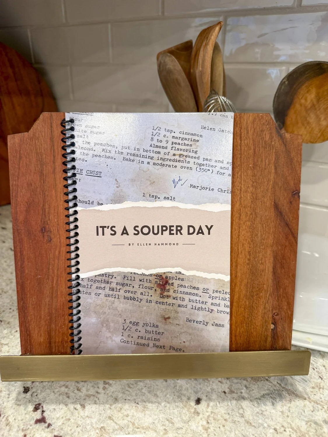 Custom designed soup cookbook leaning against a kitchen counter with the title It's A Souper Day.
