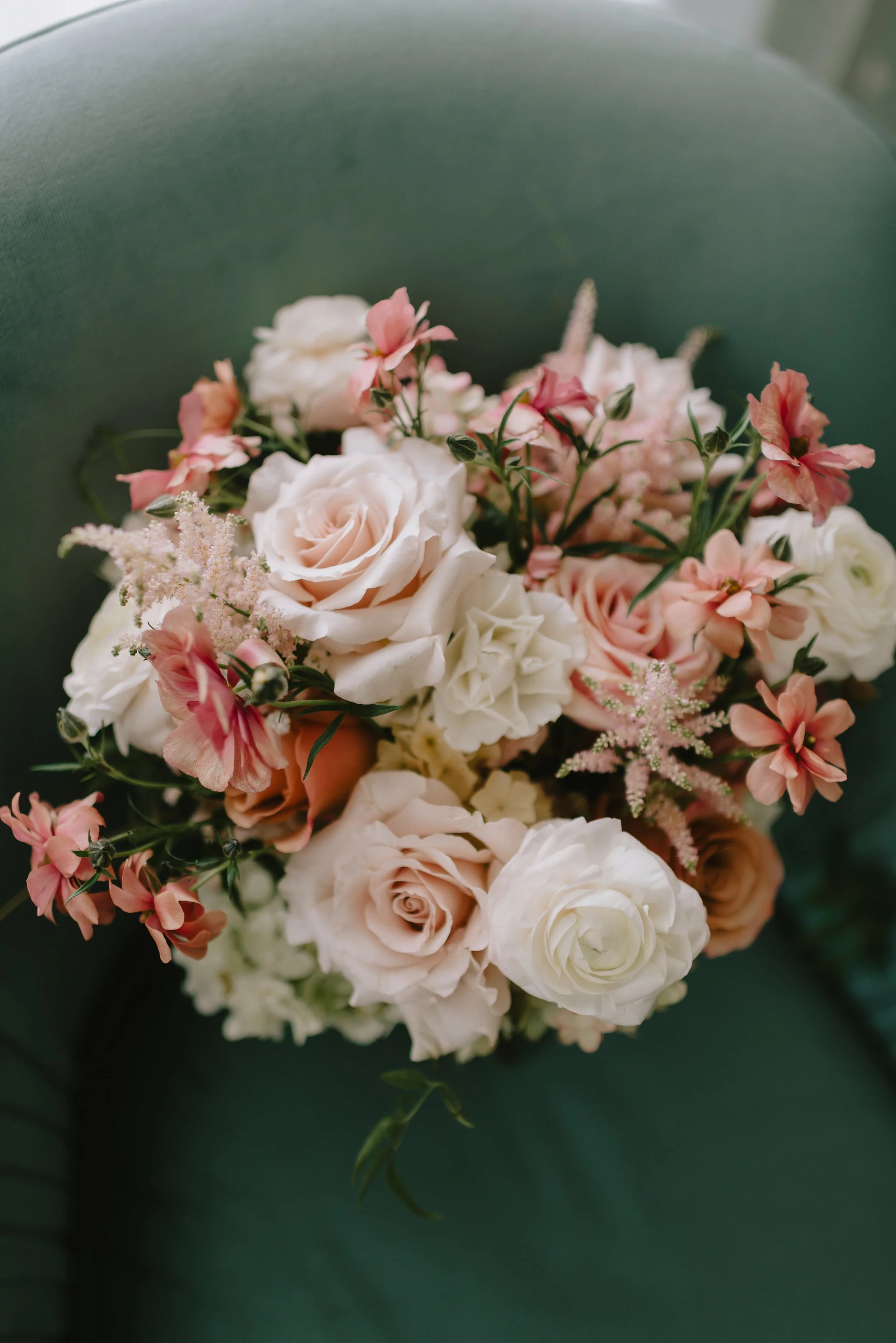 Close-up of a bouquet of light pink, white, and peach roses and various small flowers against a dark green background.