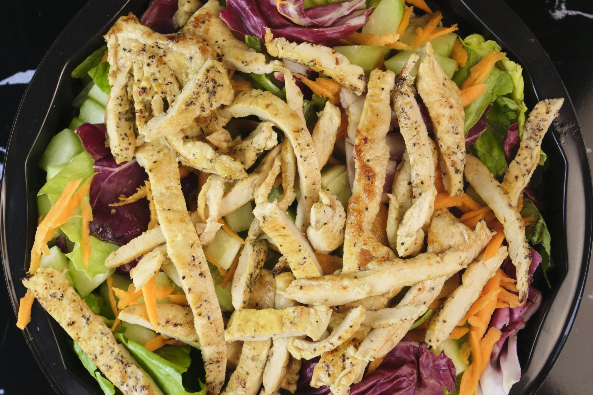 Fresh salad with shredded chicken, mixed greens, shredded carrots, and sliced cucumbers, topped with grilled chicken strips.