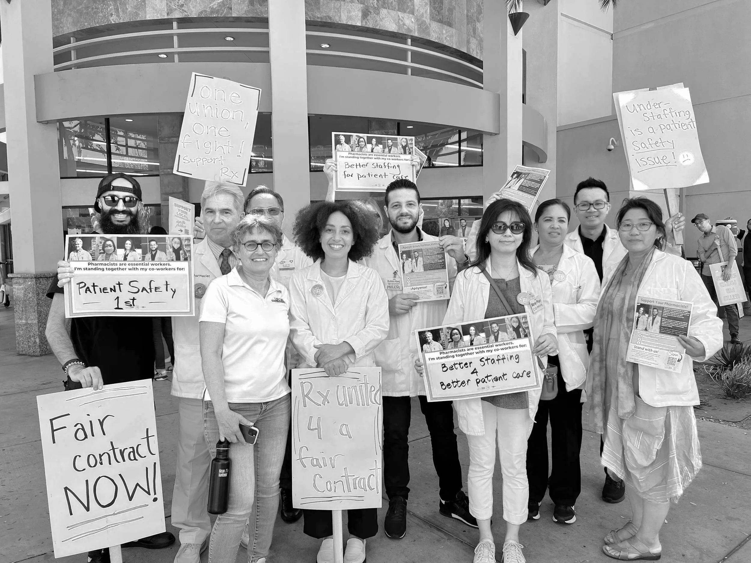 Group of healthcare workers protesting outside a building holding signs advocating for patient safety, fair contracts, better staffing, and improved patient care.