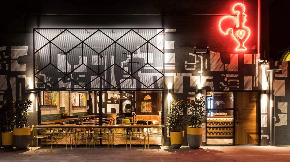 Nando's exterior of the building. Large neon sign over door and large window where we can see seating.