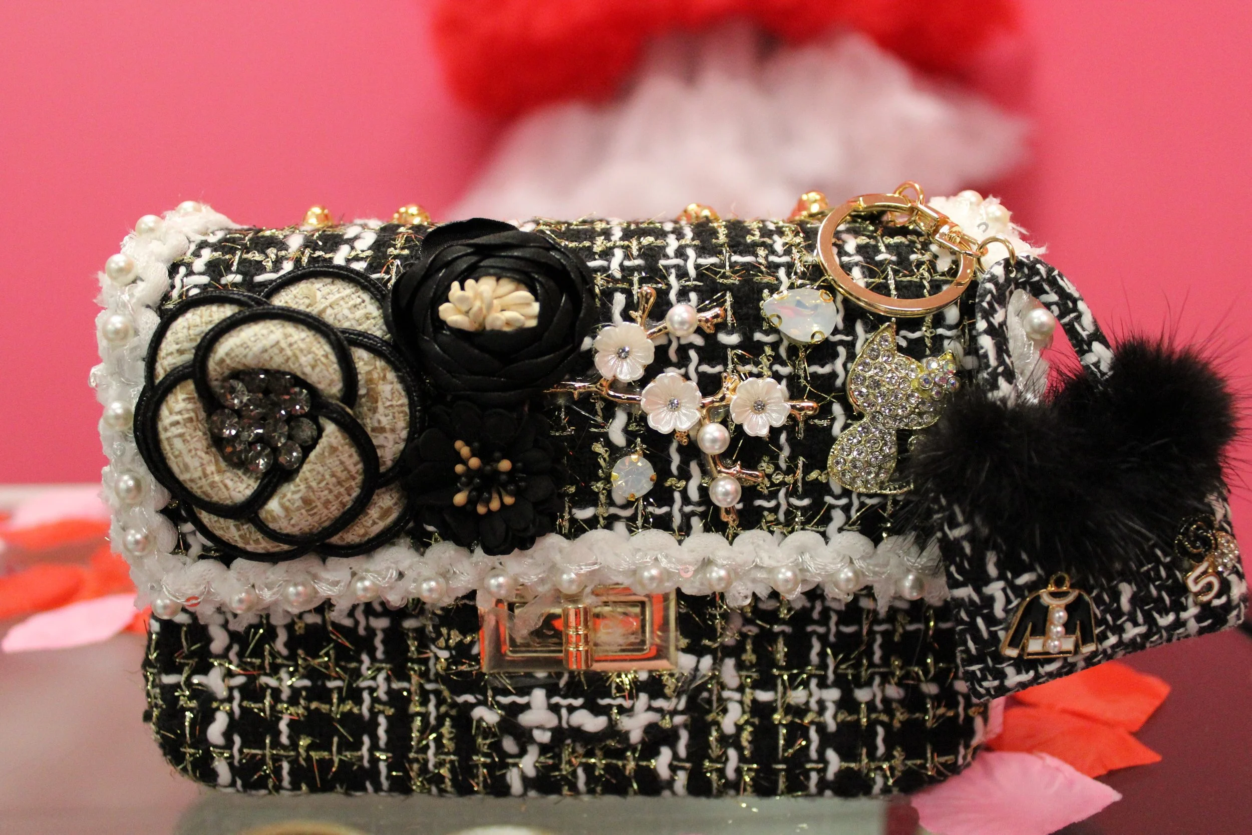 A decorative box covered in black and white fabric with various embellishments including pearls, floral appliques, rhinestones, and charms, with a pink background.