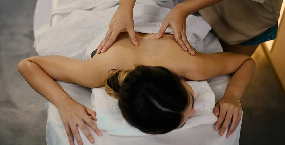 An overhead view of a patient receiving a professional therapeutic massage on their upper back and shoulders in a calm, clinical setting.