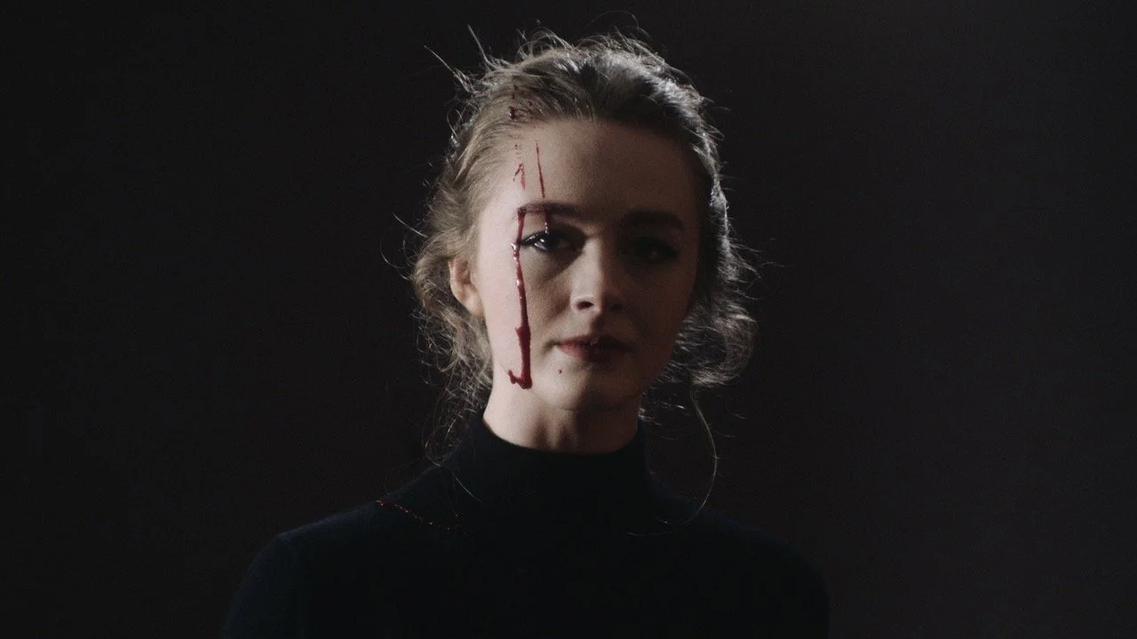 Person with blood on face, wearing black, against dark background.