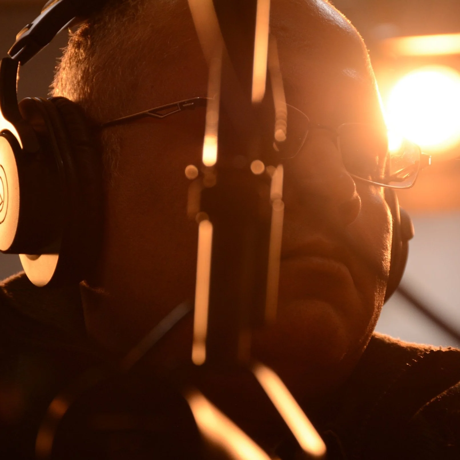 Person wearing headphones and speaking into a microphone, with warm lighting in the background.