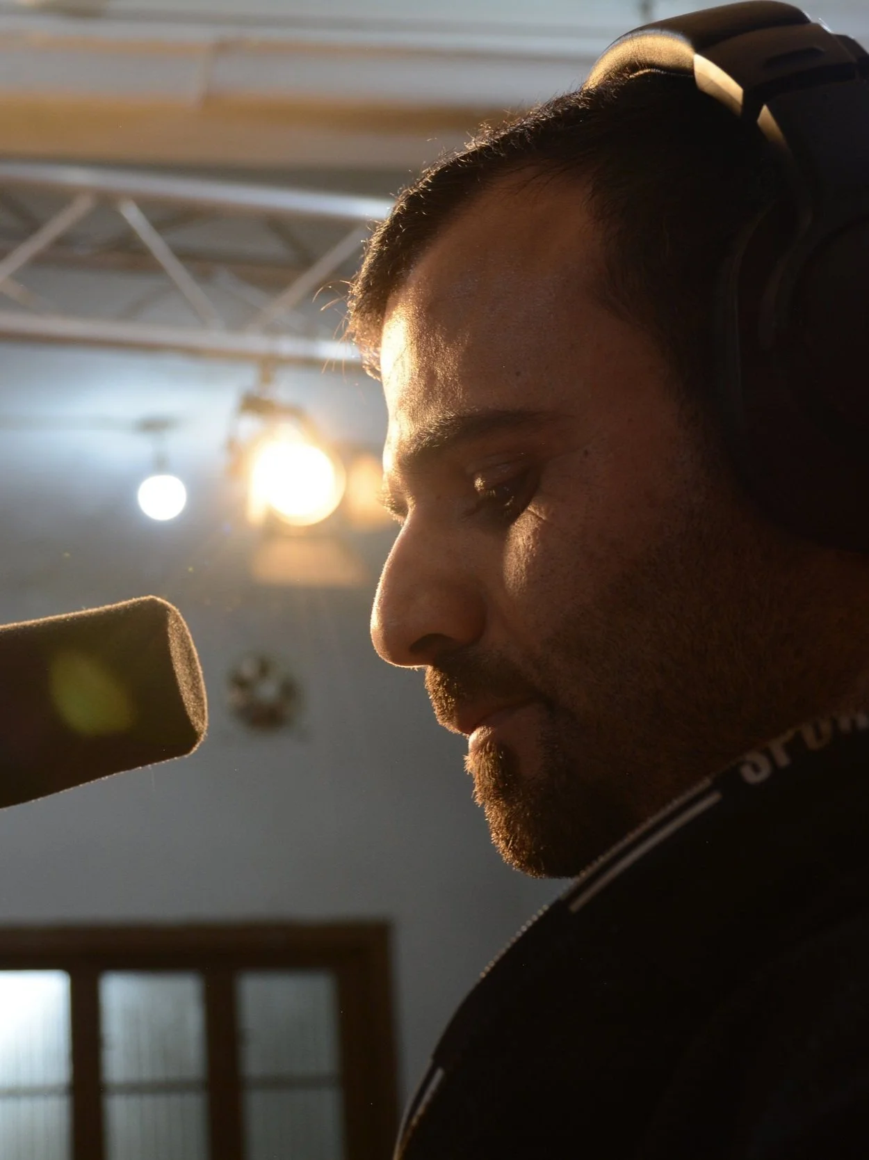 Person with headphones speaking into a microphone in a studio setting.