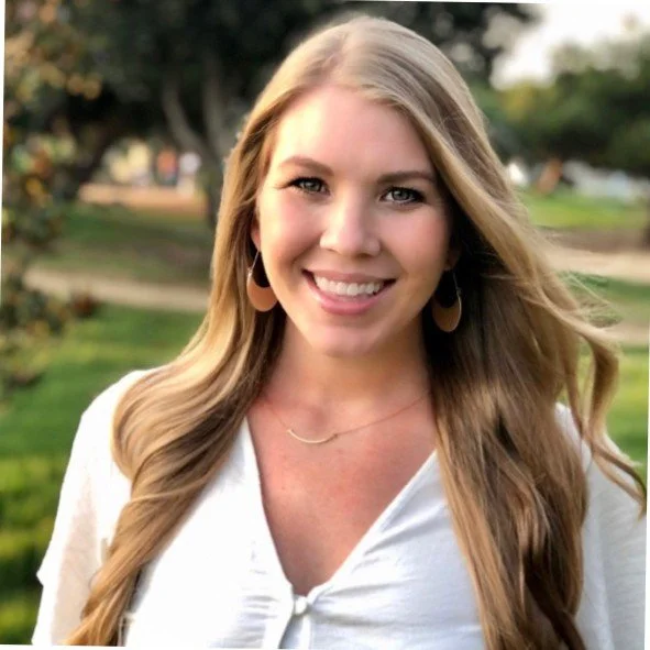 Smiling woman with long blonde hair outdoors in a park.