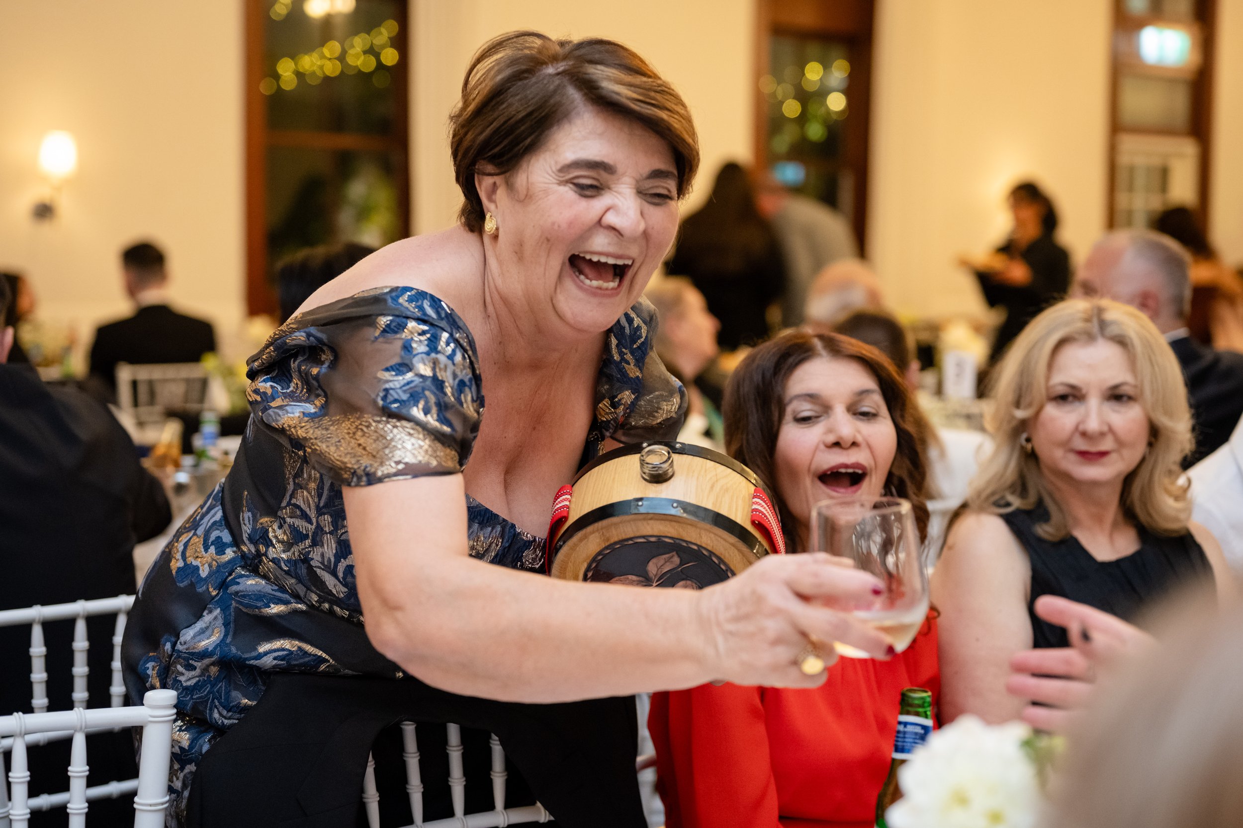 The mother of the bride laughs while pouring a drink from a small keg at the Cropley House reception in Baulkham Hills