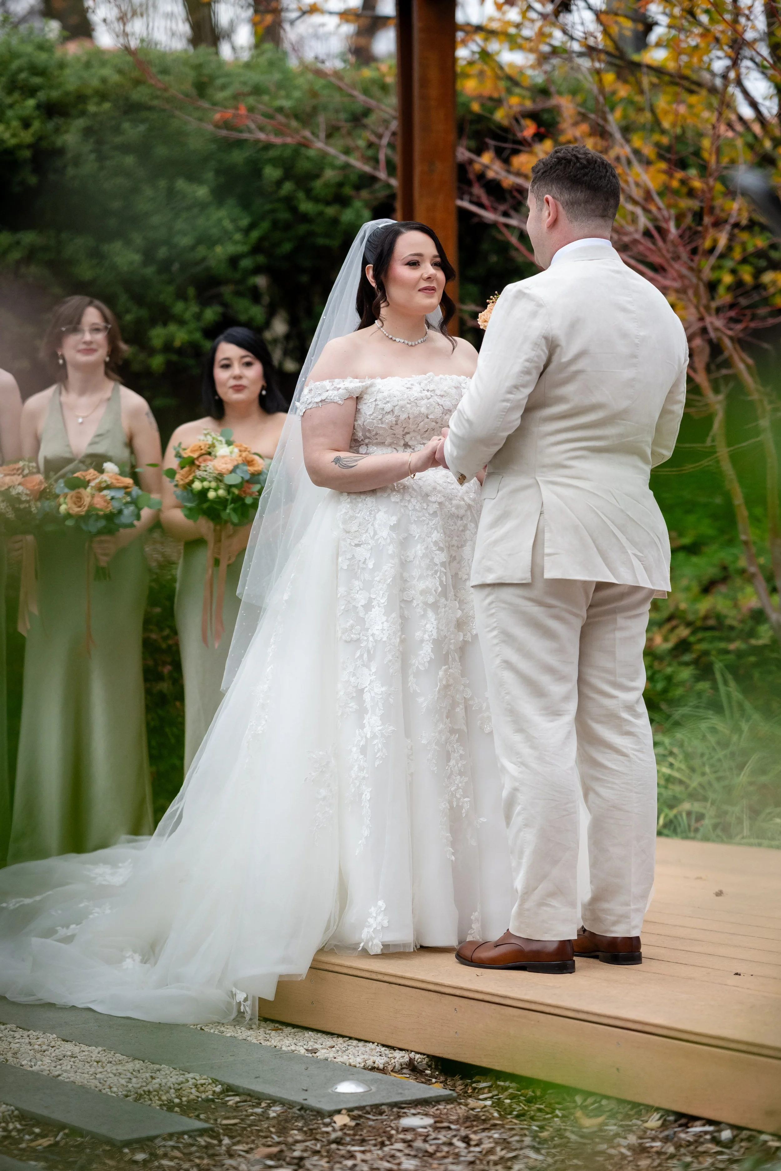 Bride and groom hold hands during their ceremony at the Brassey Hotel in Canberra, bridesmaids watching behind them