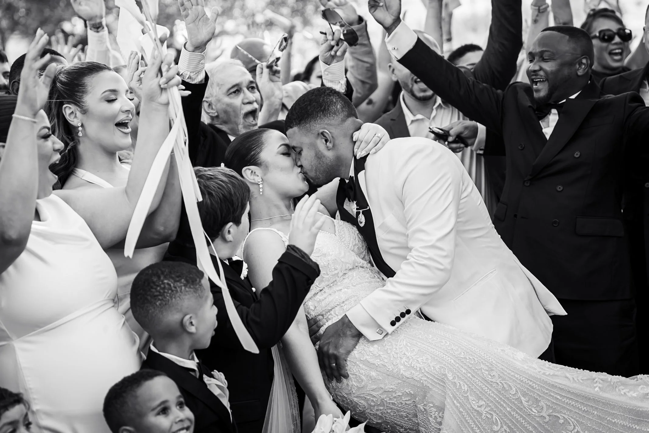 Guests raise ribbon wands and cheer as the bride and groom kiss surrounded by family at their Shaw Estate wedding in Murrumbateman