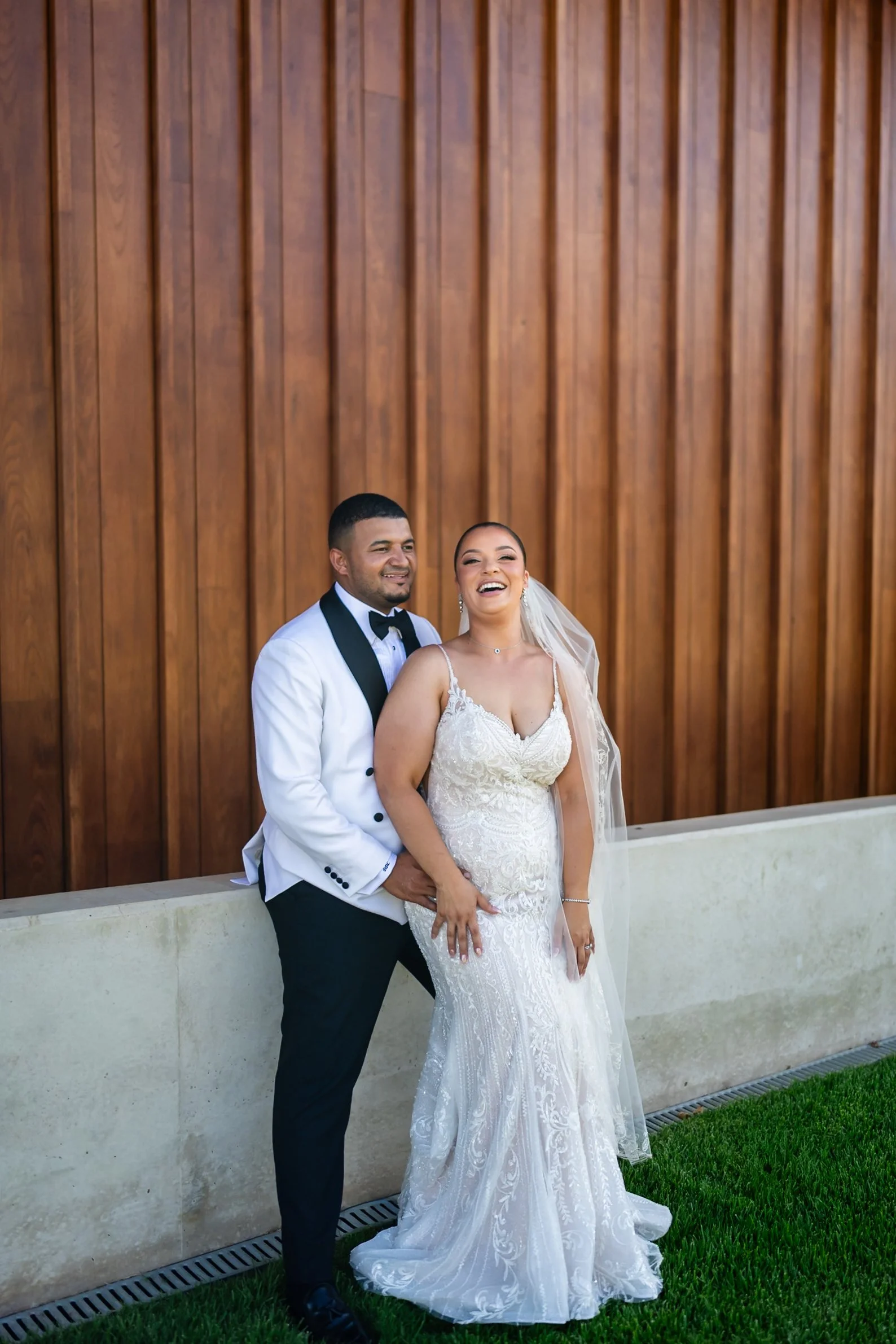 Bride and groom stand together against a timber wall on the lawn at Shaw Estate, Murrumbateman