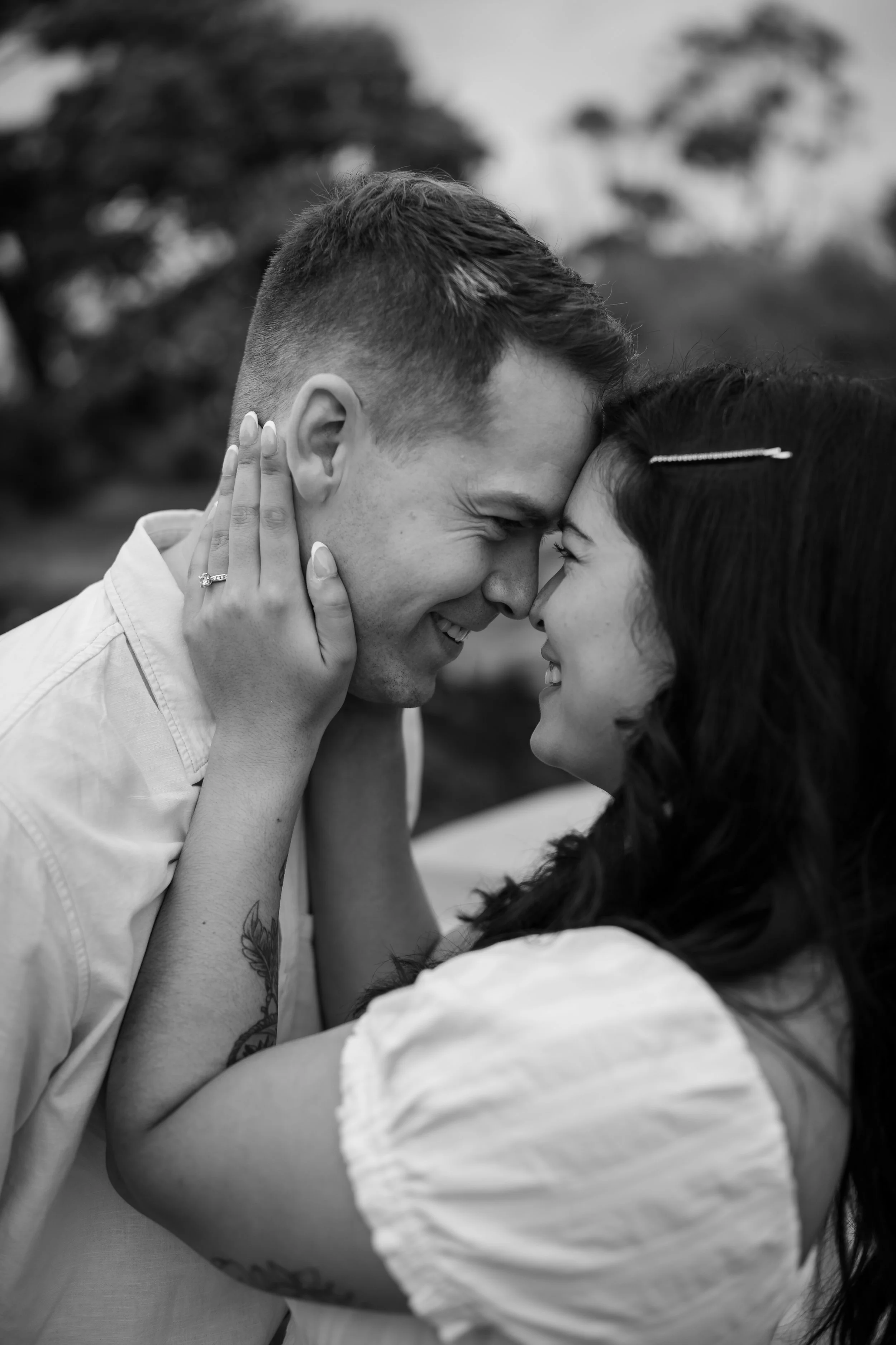 A black and white photo of a couple touching foreheads and smiling, with the woman gently holding the man's face.