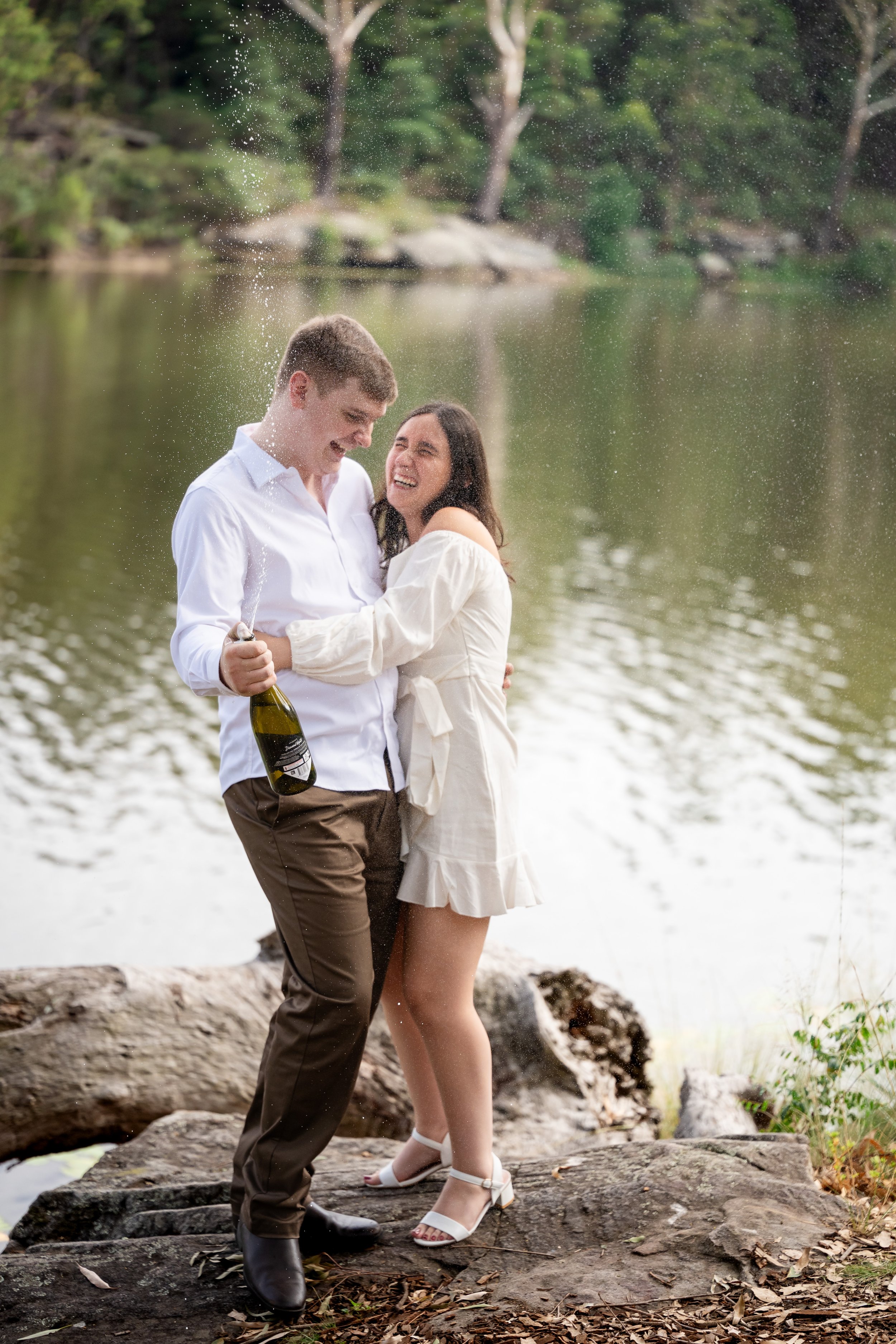 A couple at the lake celebrating with champagne, smiling and laughing.