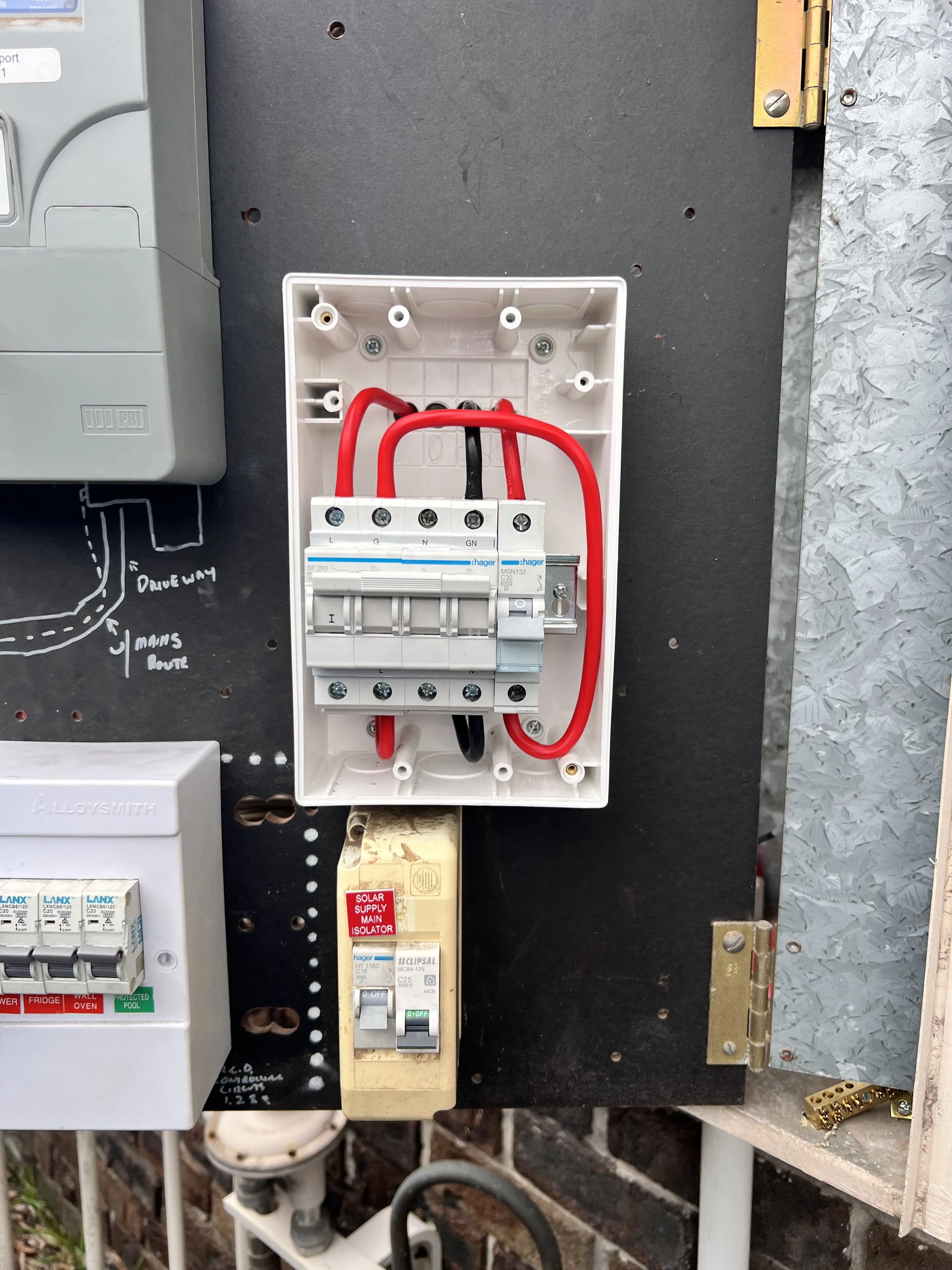 Electrical panel with red and black wires connected to a circuit breaker, mounted on a black board with handwritten notes and drawings, and surrounding electrical components. For generator supply